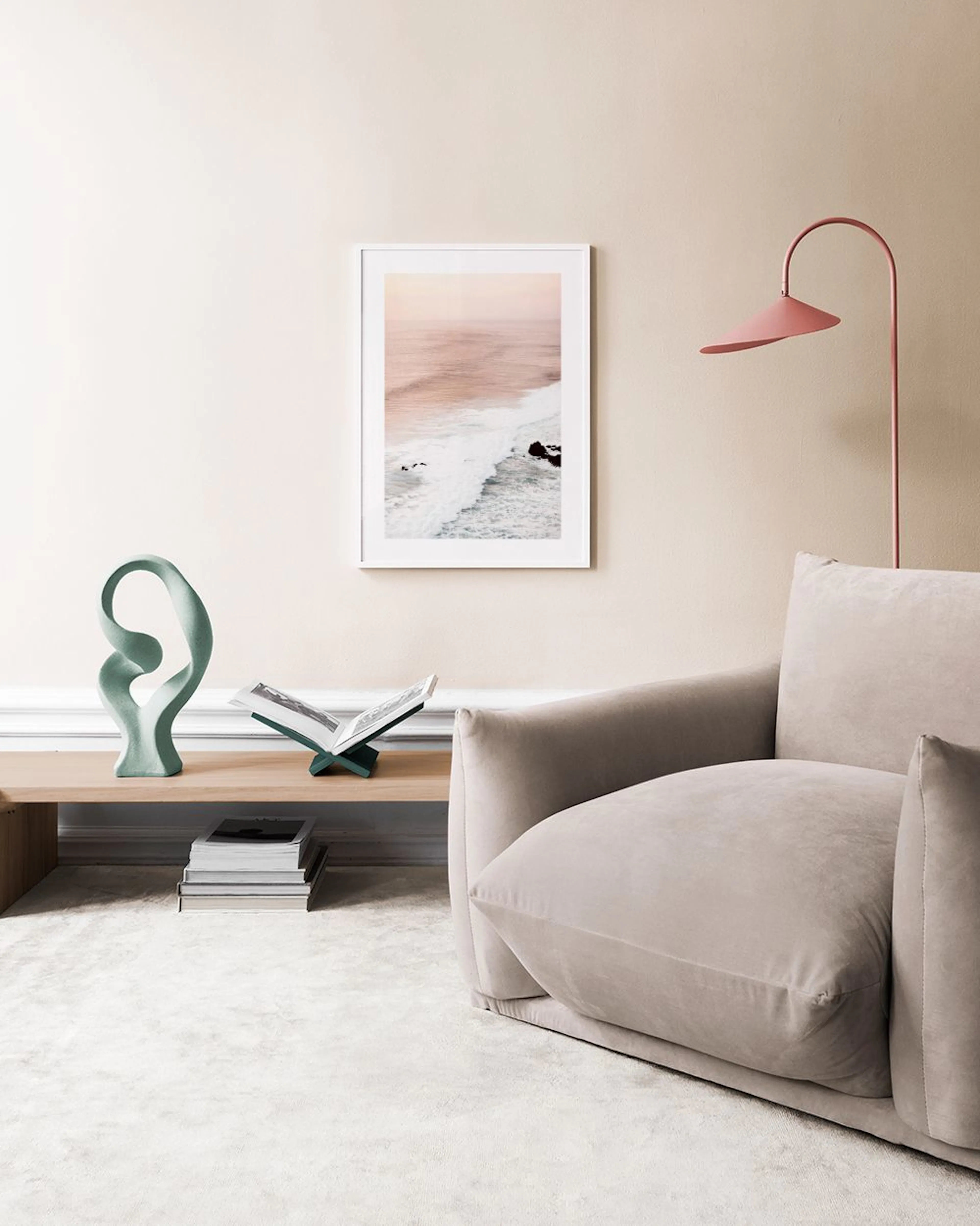 A coastal print with soft waves and rocks, displayed on a warm gray wall above a black table with a sculpture.
