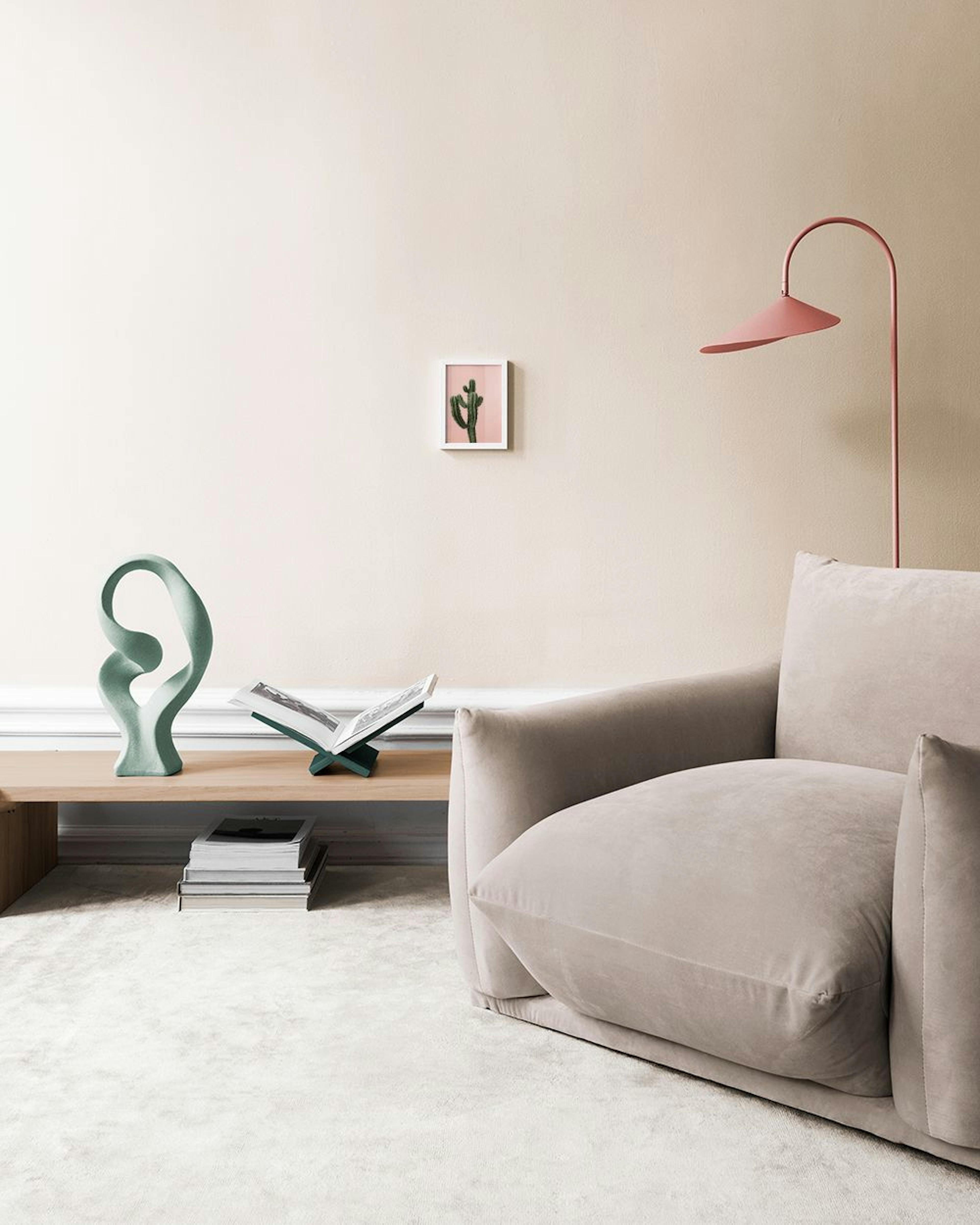 Affiche murale dun cactus vert sur fond rose clair, au-dessus dun banc rose avec coussins.