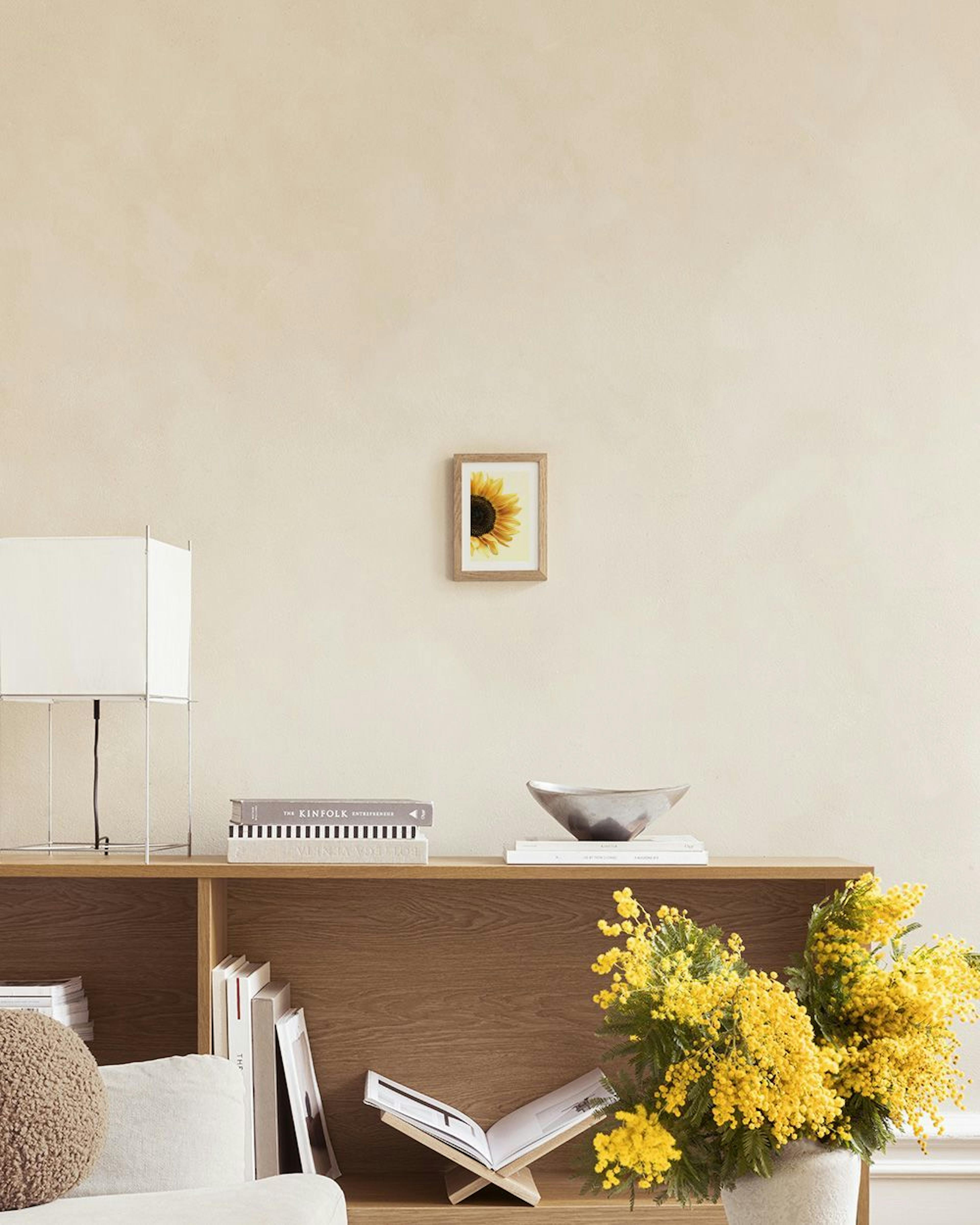 A sunflower print with yellow petals and a dark center, hanging above a green velvet chair with a yellow cushion.