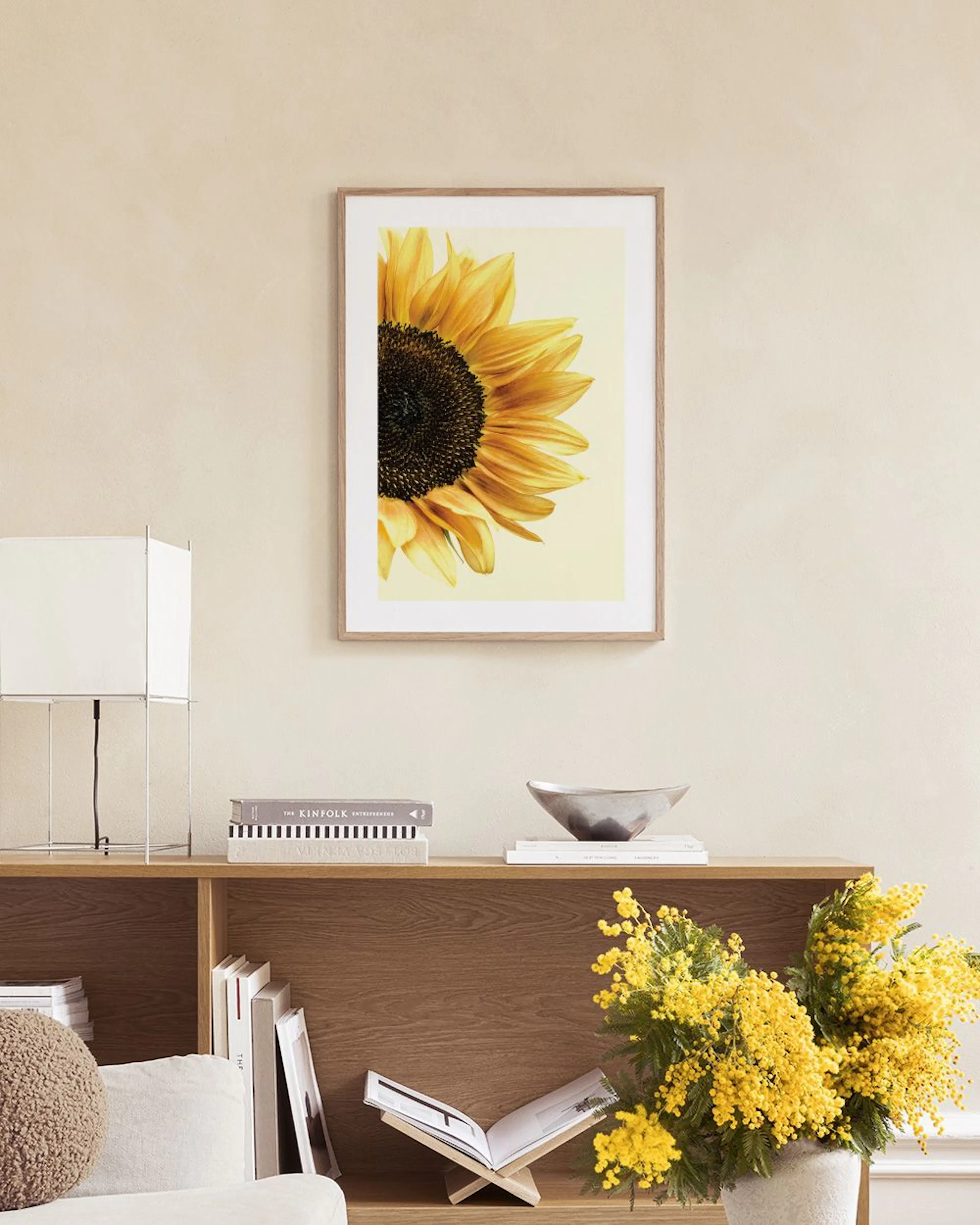 A sunflower print with yellow petals and a dark center, hanging in a room above a green velvet chair.