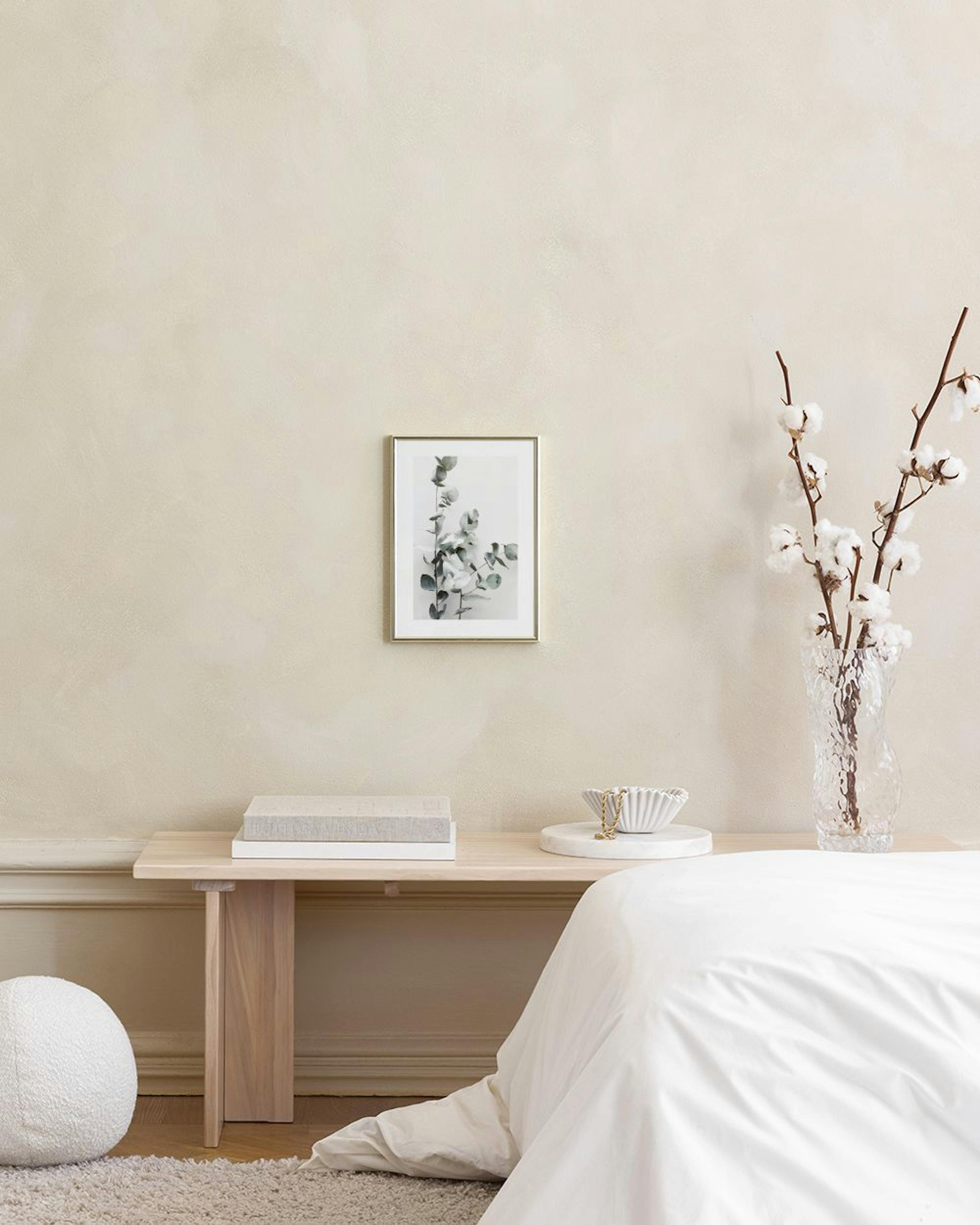Poster van eucalyptus takken in zwart-wit, hangend boven een roze poef en grijze kubussen.