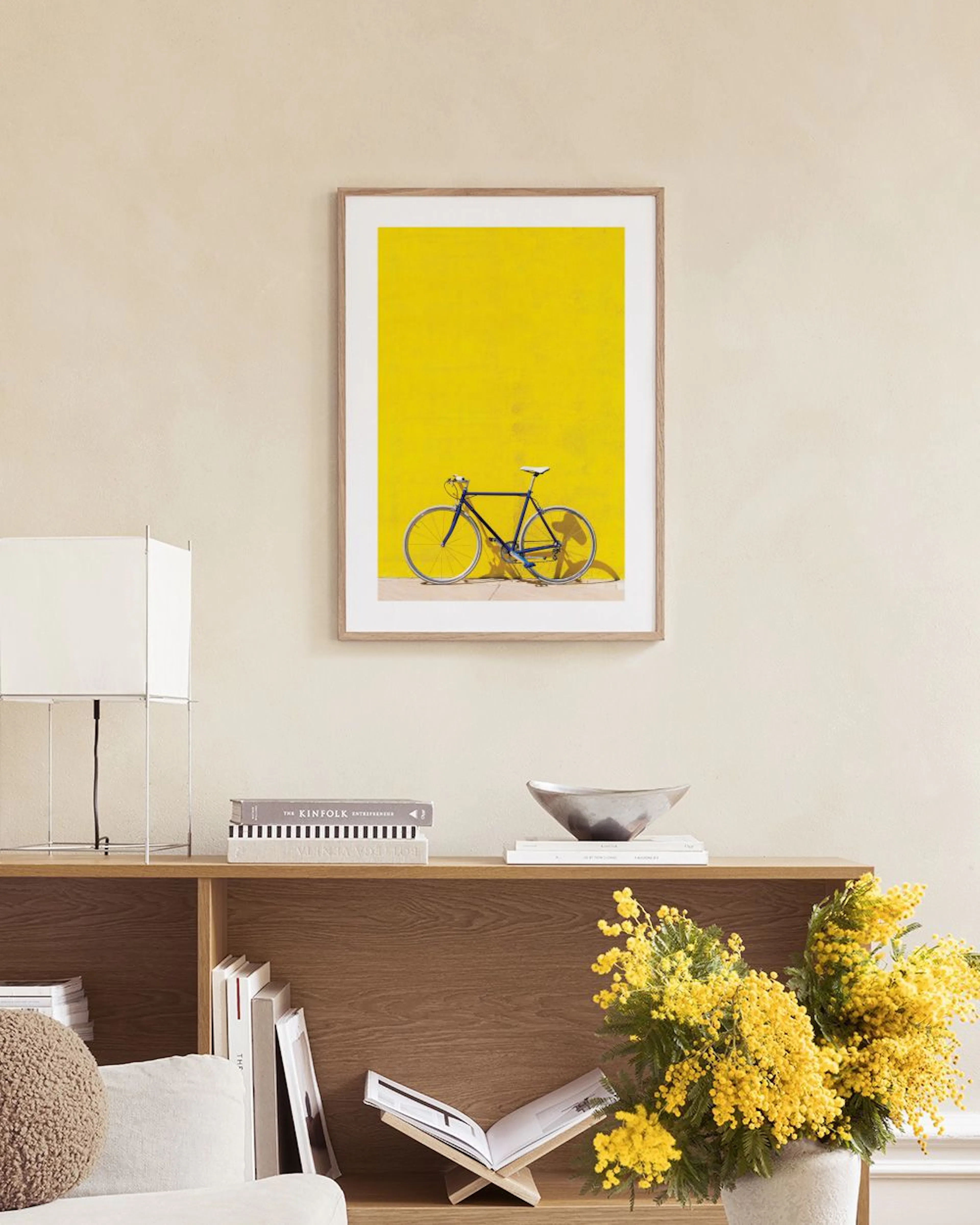 Plakat z czarnym rowerem na tle intensywnie żółtej ściany, wyeksponowany nad czarną konsolą w nowoczesnym wnętrzu.