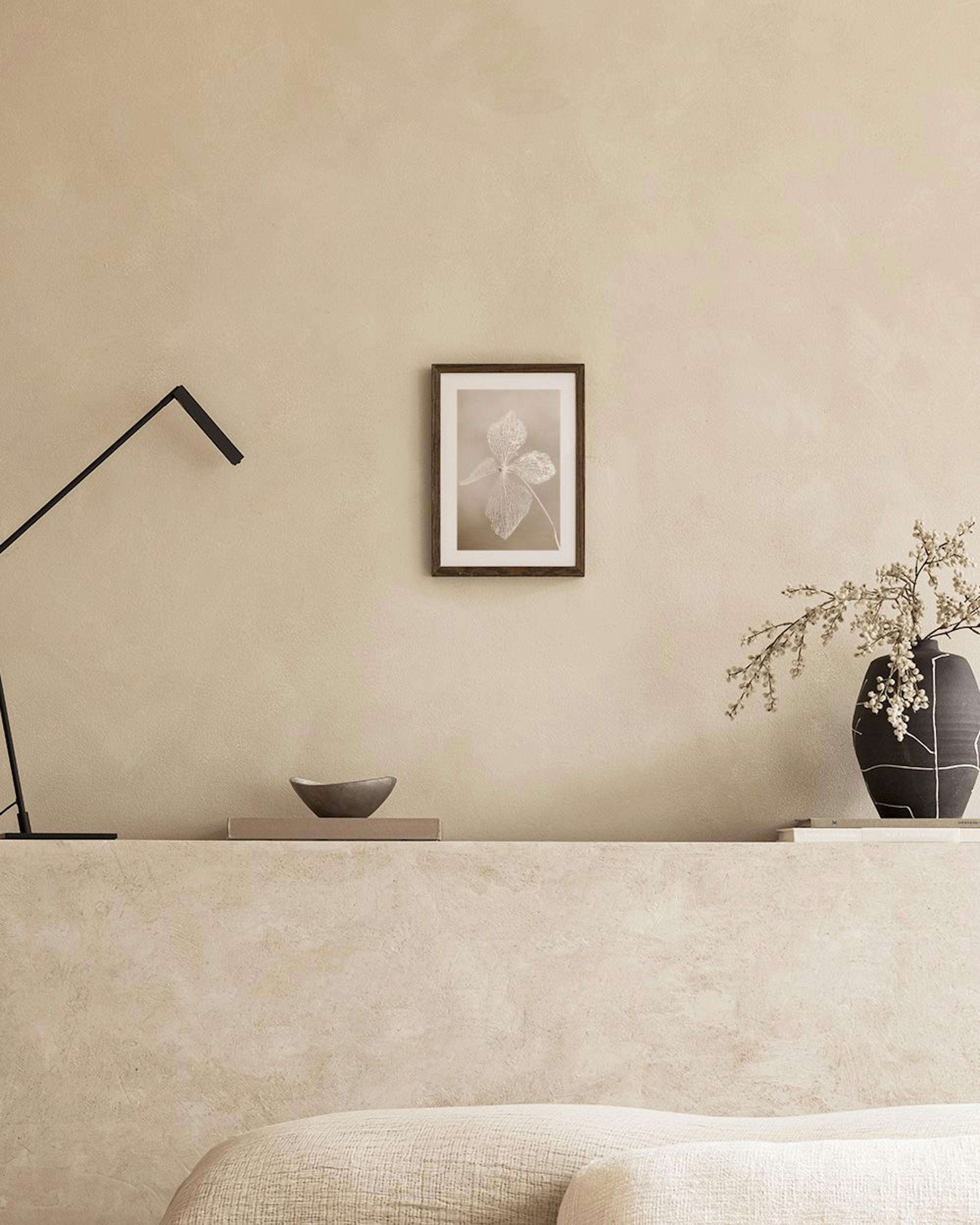 Poster van een witte, gedetailleerde bloem op een beige achtergrond, hangend boven een zwarte console tafel met lamp en decorati