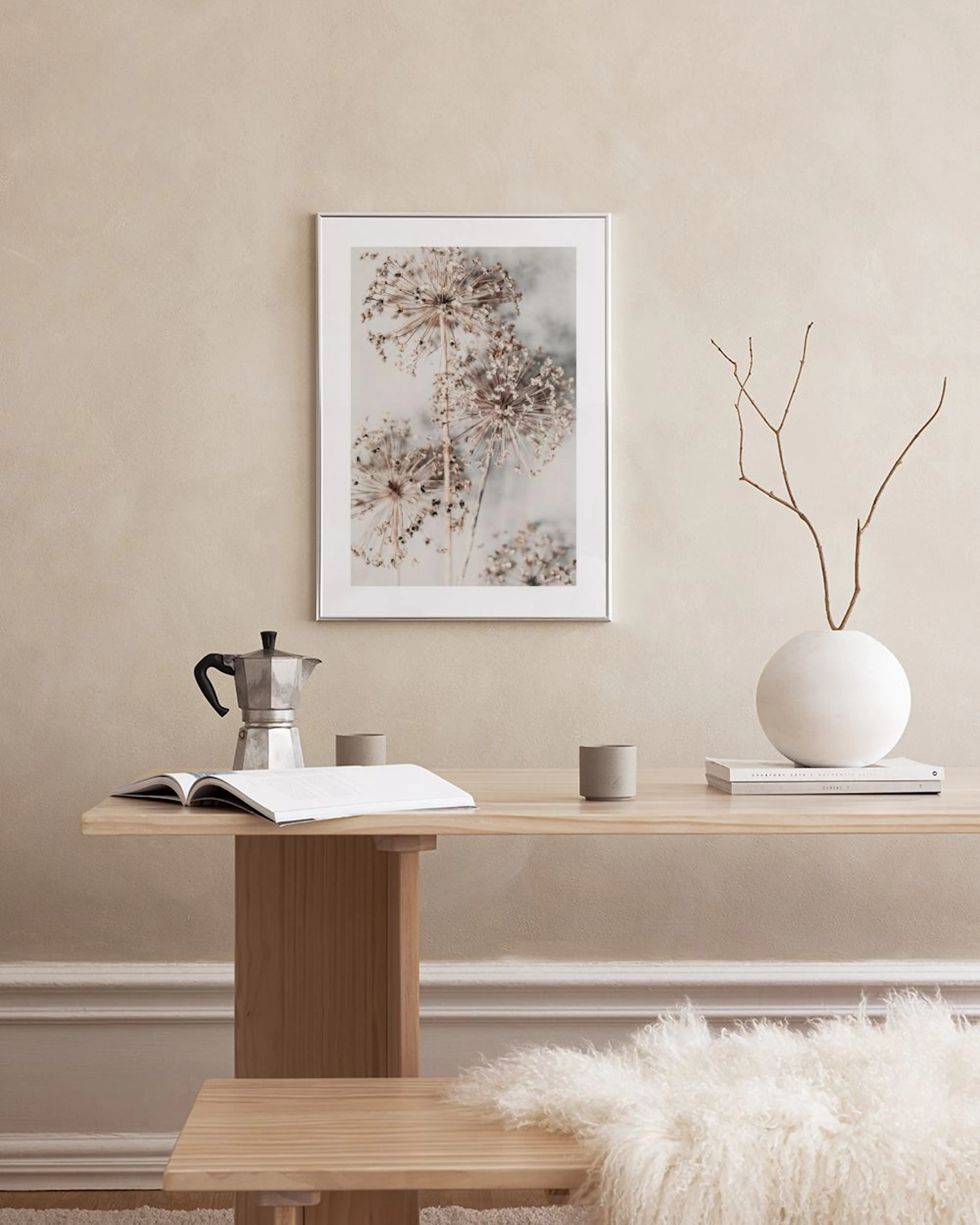 Poster met gedroogde allium bloemen in neutrale tinten, hangend in een modern interieur boven een bruine poef.