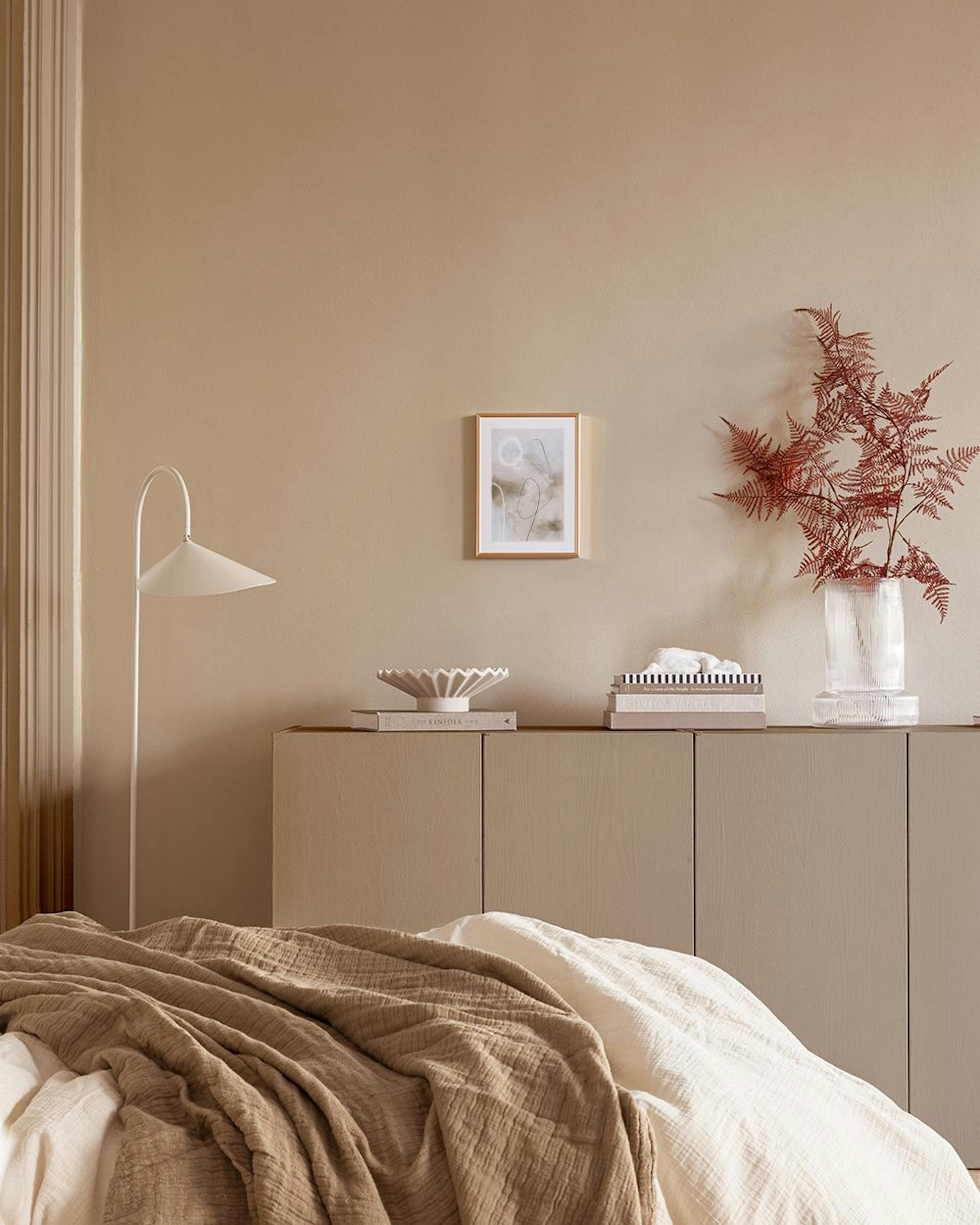 Abstrakter Poster mit beigen, grauen und weißen Farbfeldern, feinen Linien und Kreisen, über einem Sideboard mit Büchern und Lam