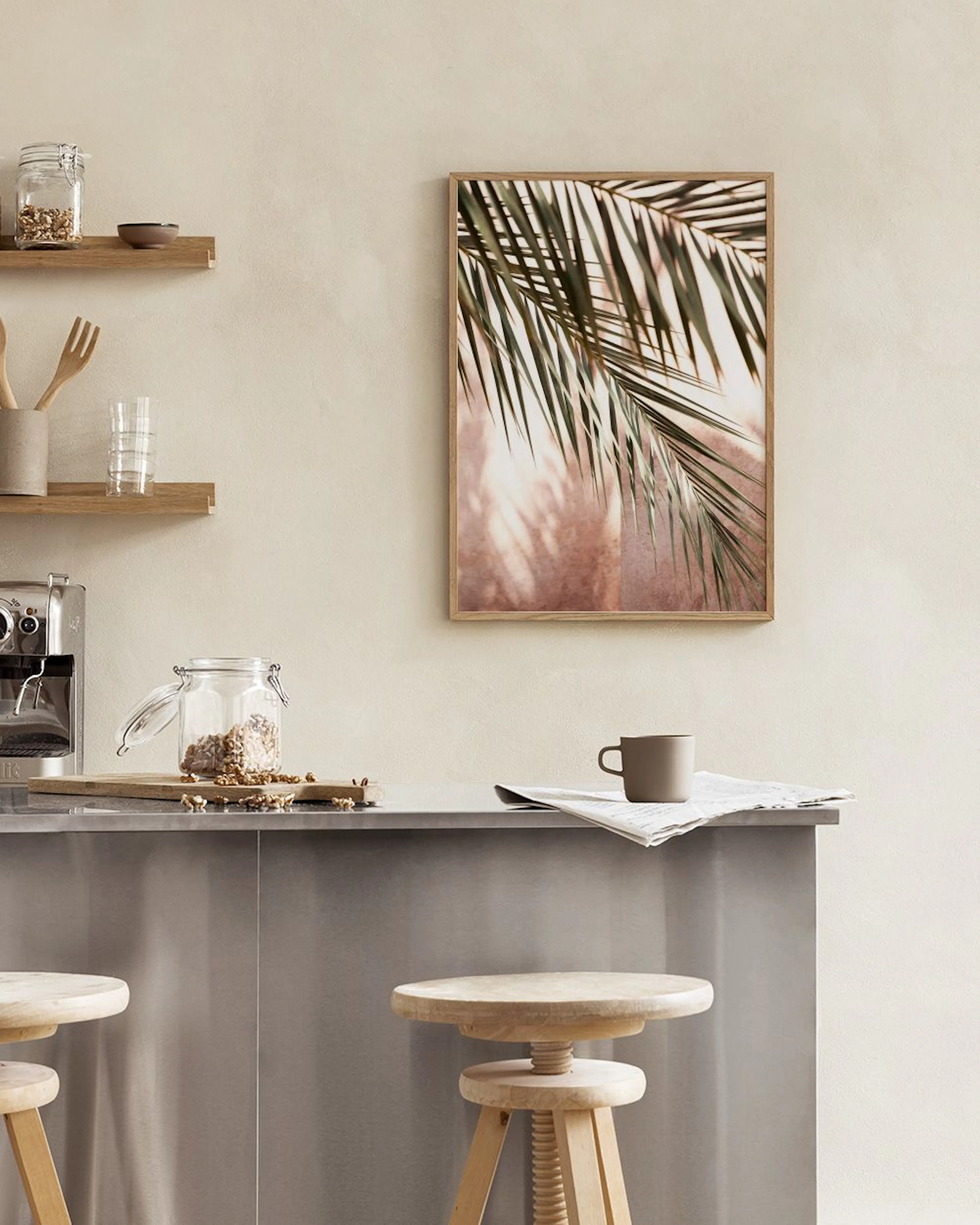 Poster mit grünen Palmblättern hängt über einem Rattan-Sideboard mit Vasen und Büchern in einem modernen Raum.