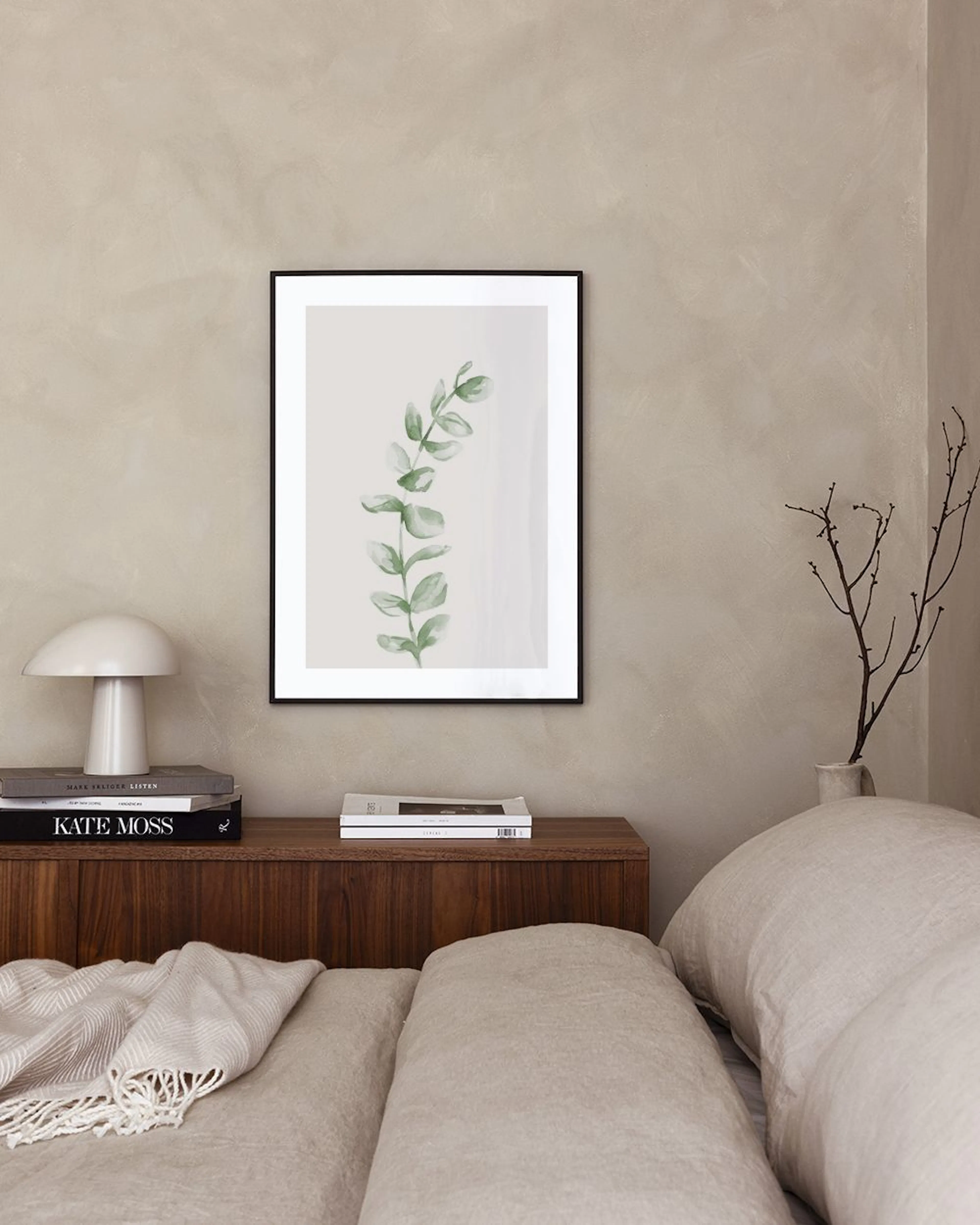 Botanical print of a green eucalyptus branch, hanging above a shelf with a white bowl and textured vase.