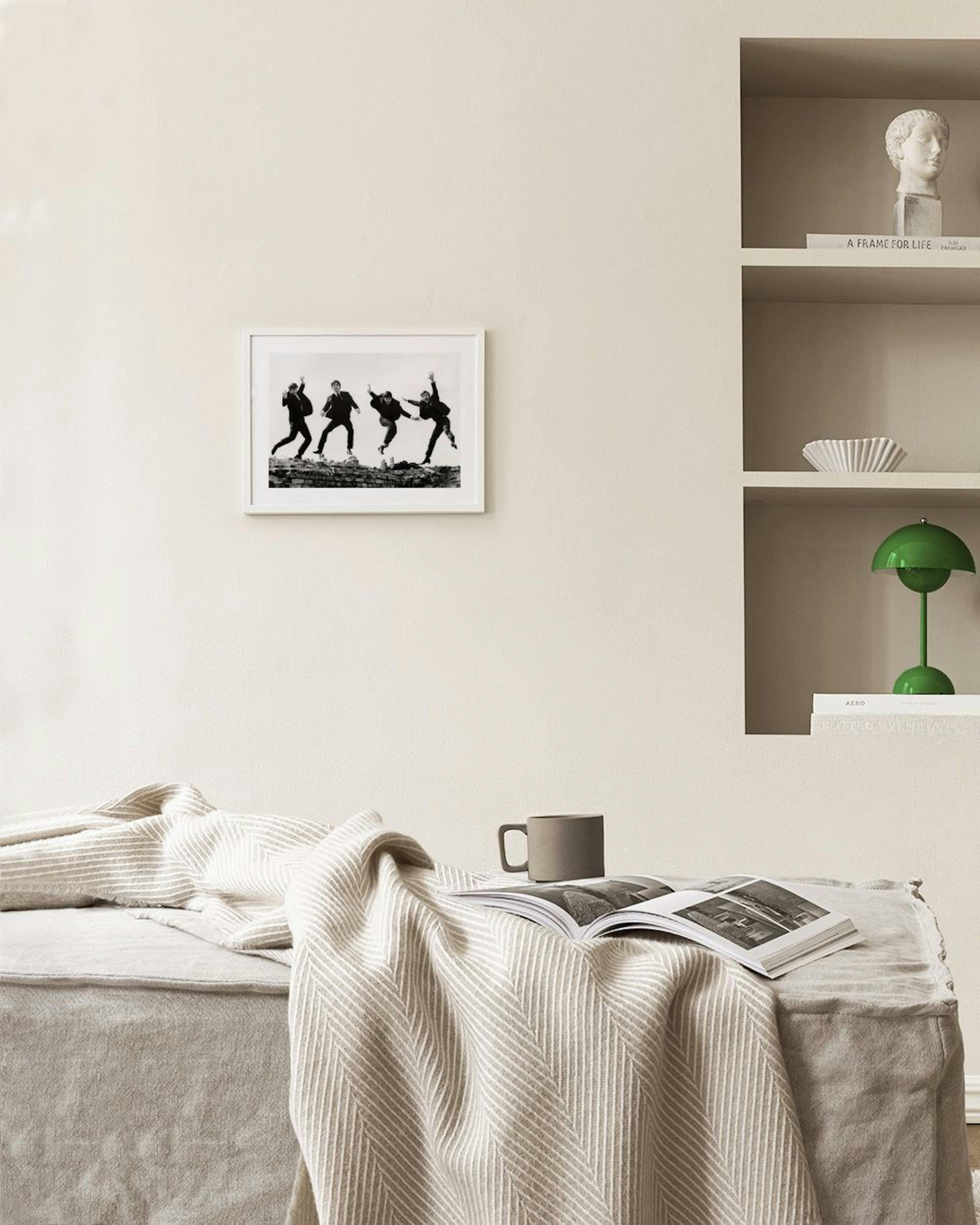 Schwarz-weiß Poster der Beatles beim Springen, über einem Beistelltisch und Sessel im Wohnzimmer.