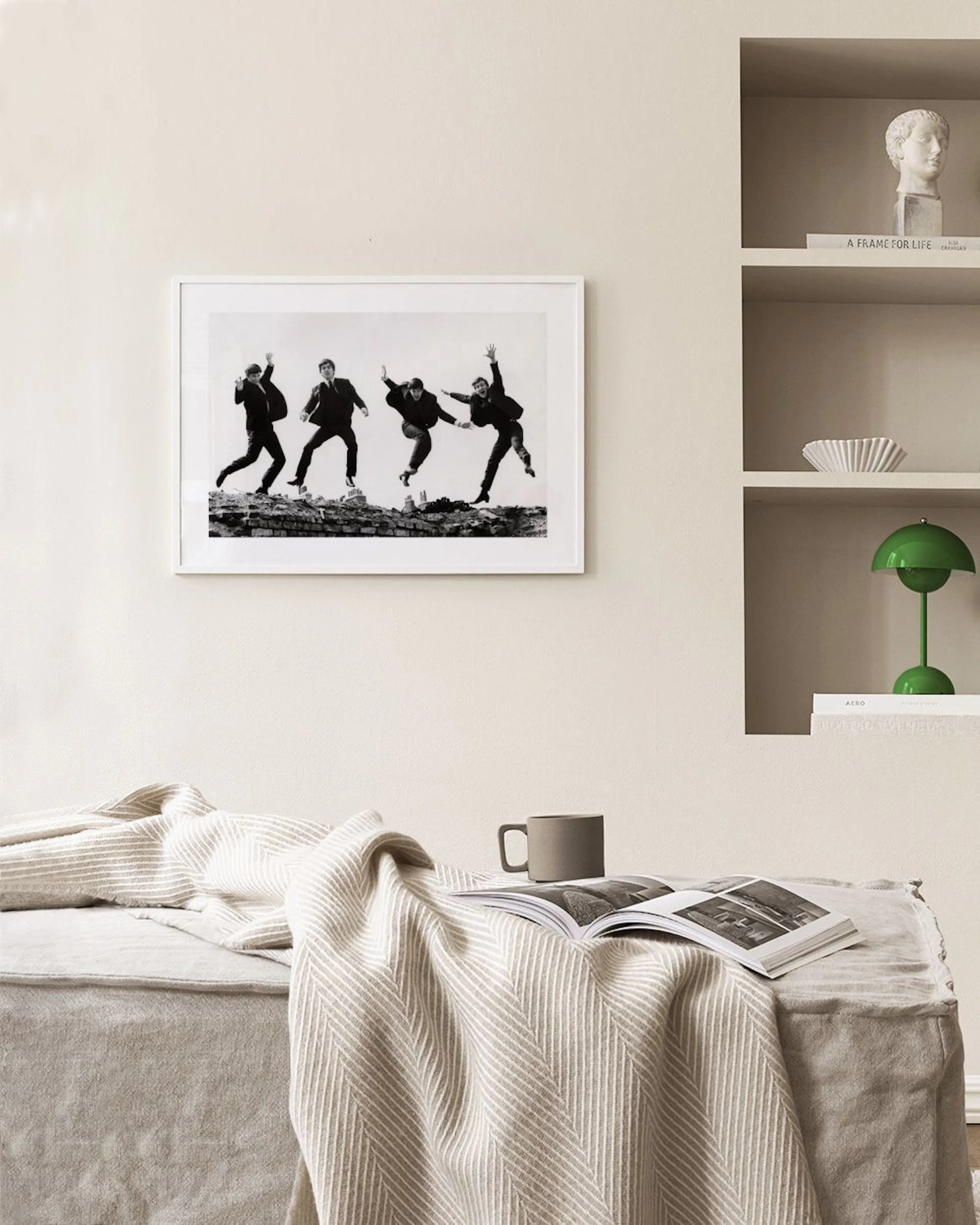 A black and white print of The Beatles jumping, displayed on a light grey wall above a side table and navy armchair.