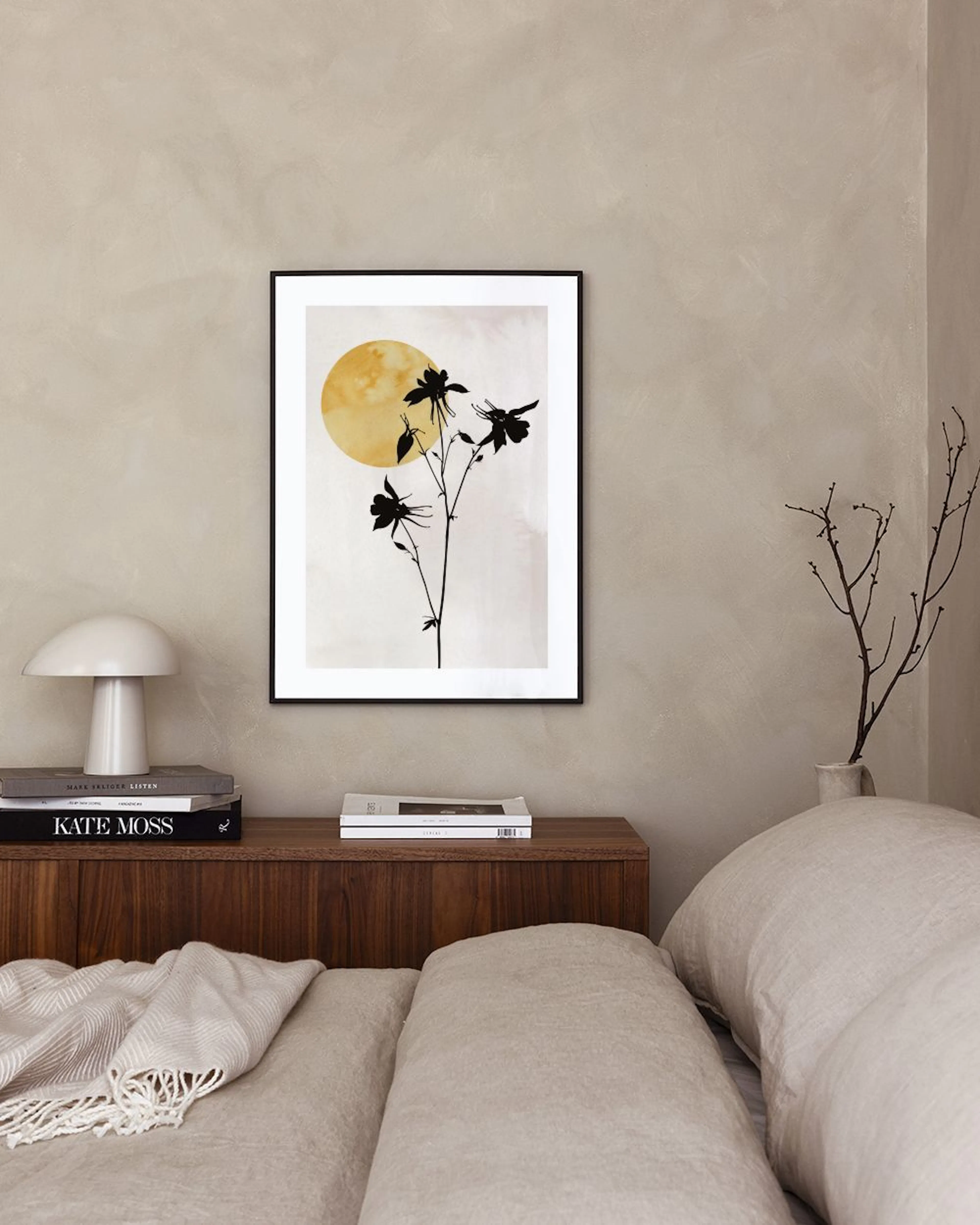 A print of black flower silhouettes against a yellow sun and light background, displayed in a modern room with a brown velvet ch