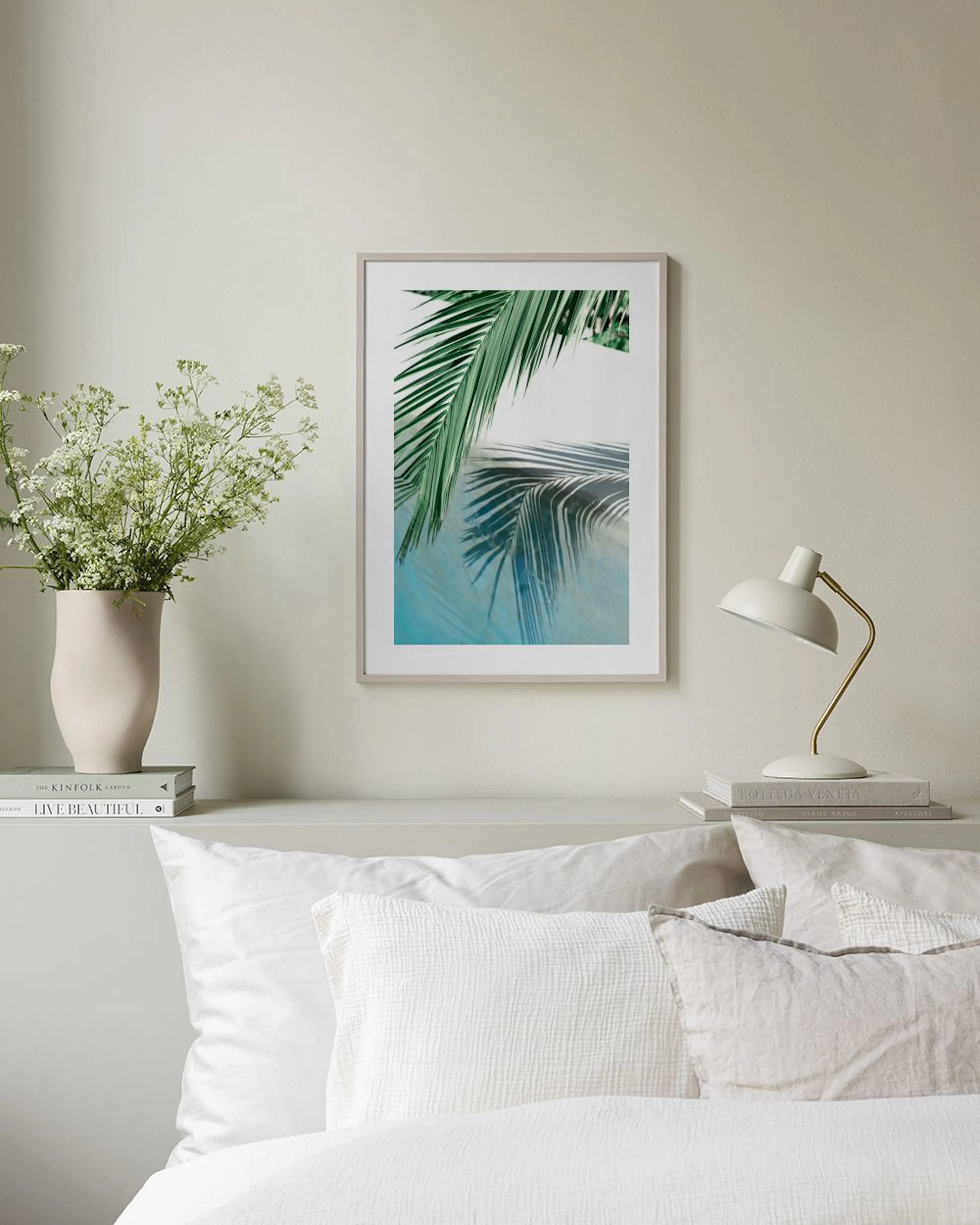 Póster de hojas de palmera verdes reflejadas en agua azul, colgando sobre un banco de madera con libros.