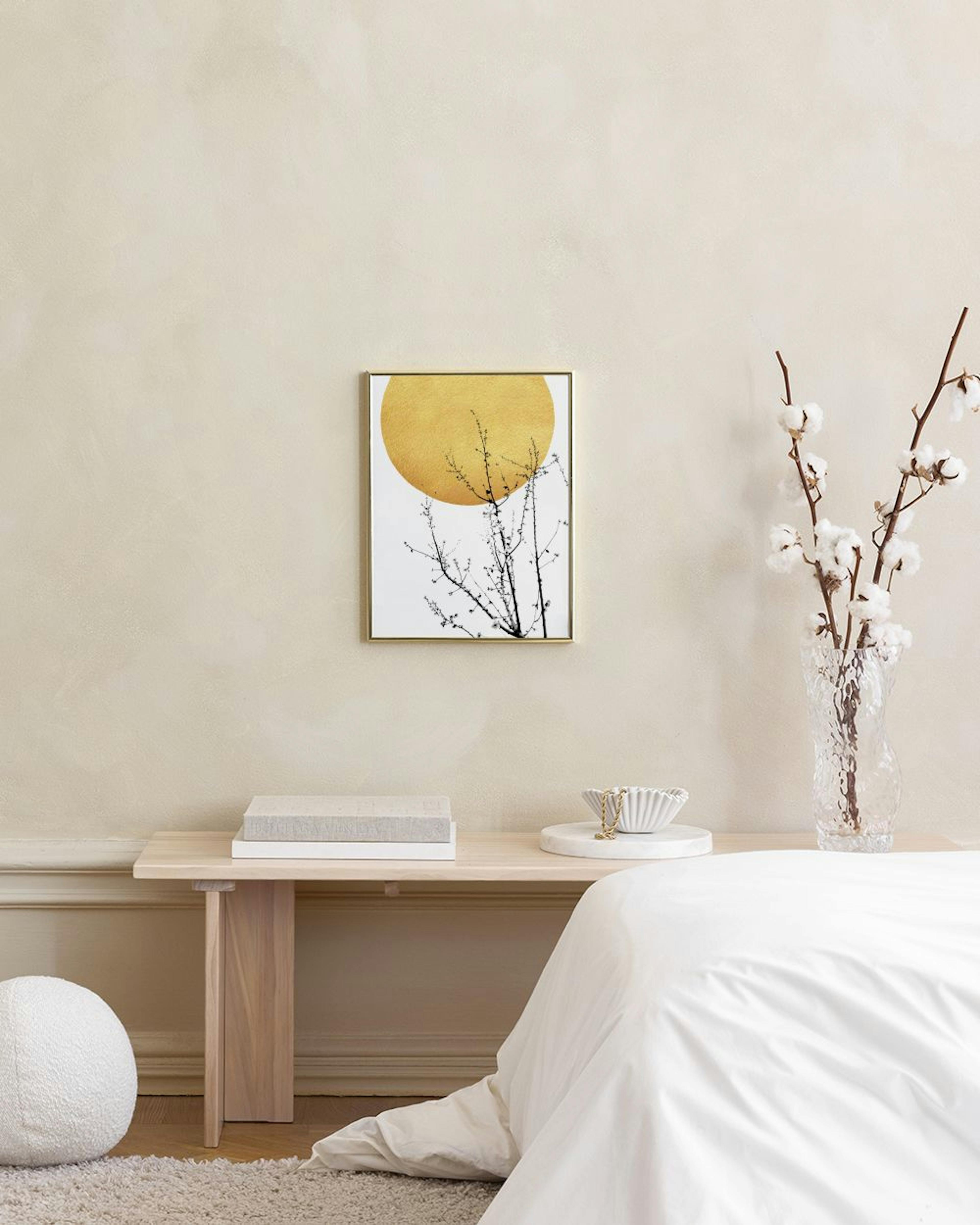 Póster de árbol con ramas y un sol dorado sobre fondo blanco, colgado sobre un taburete con libros en una habitación.