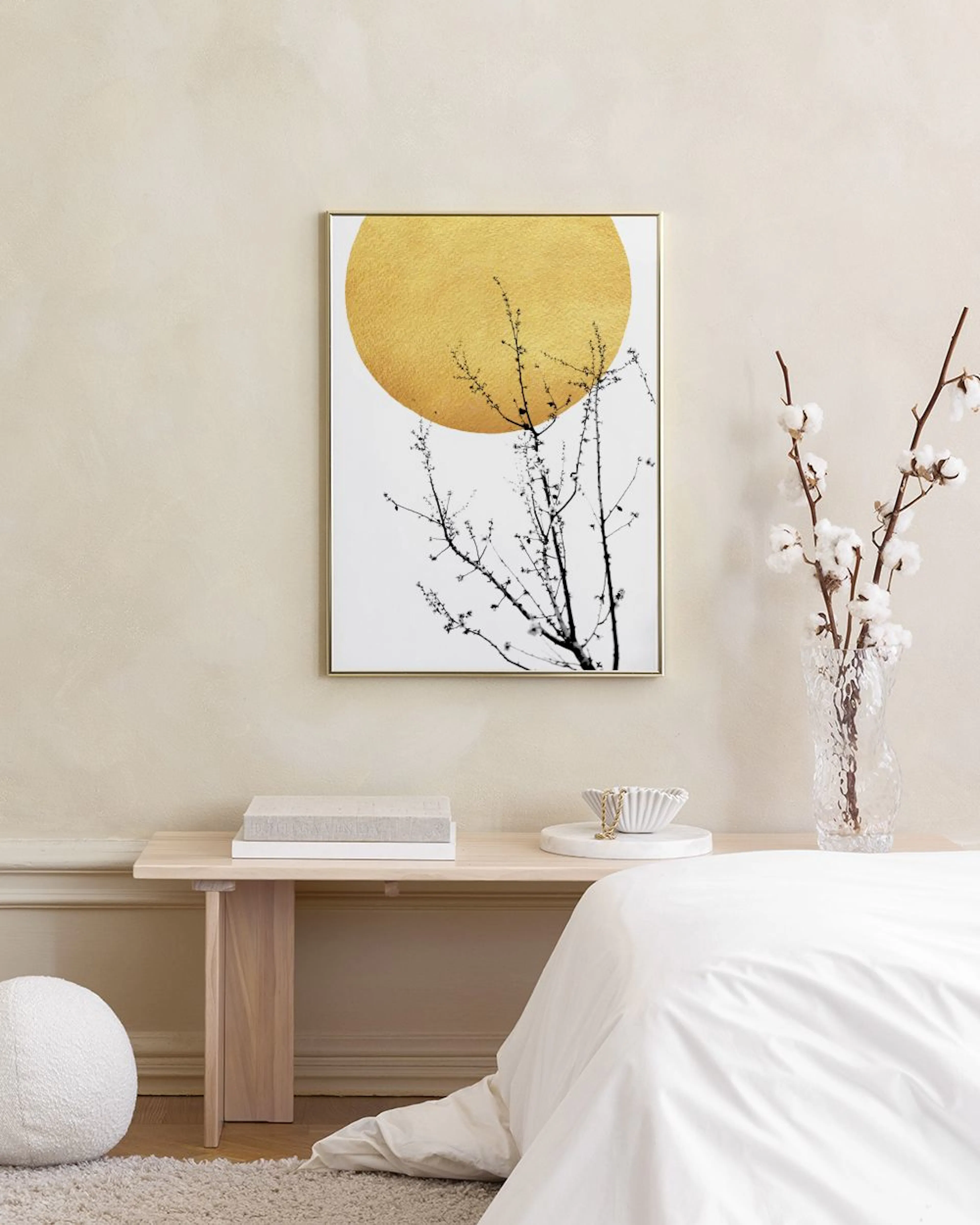 A print of a golden sun and black-and-white tree branches, hanging above a small cork stool with books in a grey and white room.