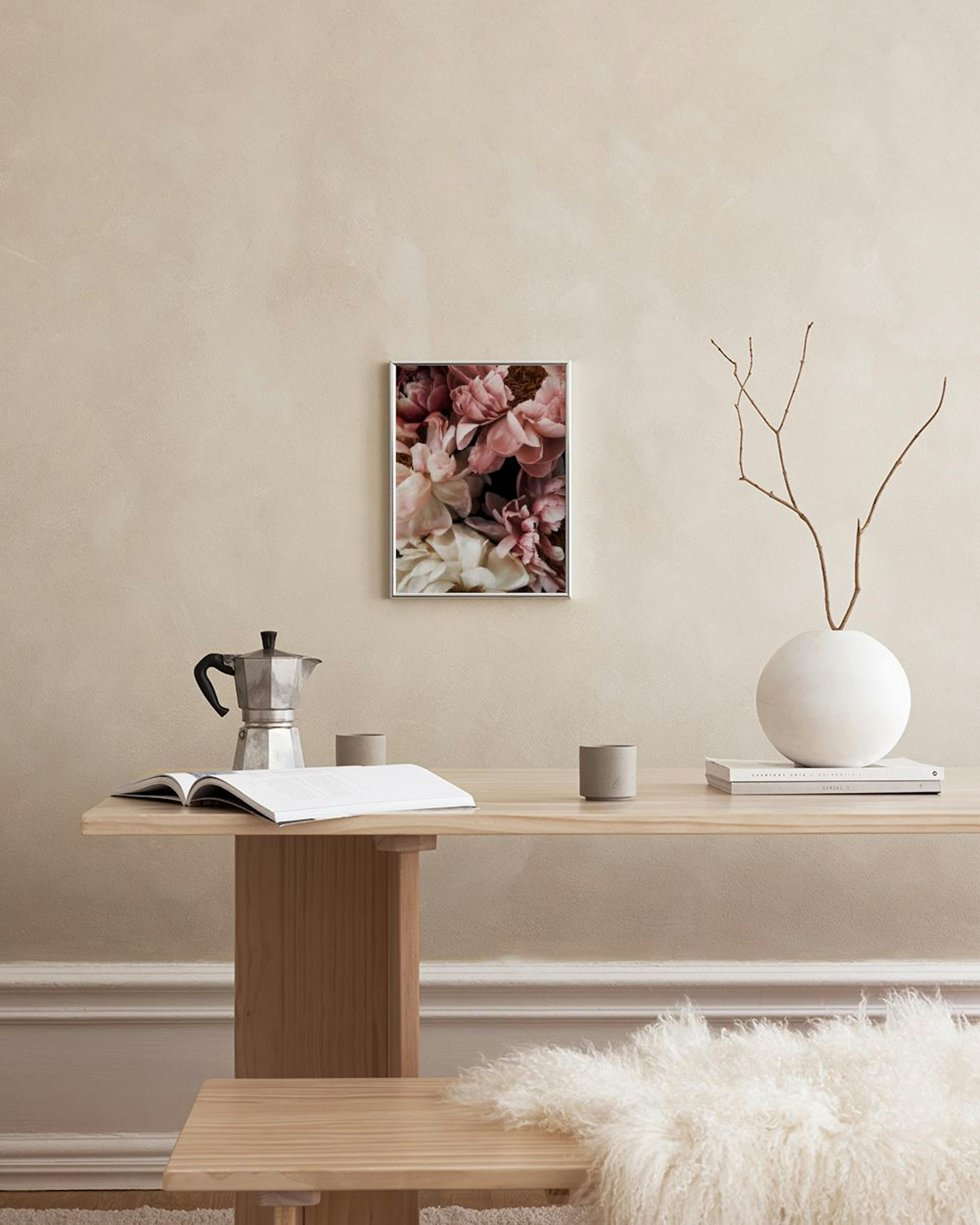 Juliste vaaleanpunaisista ja valkoisista pioninkukista ripustettuna lipaston yläpuolelle, jossa on maljakoita ja kirjoja.