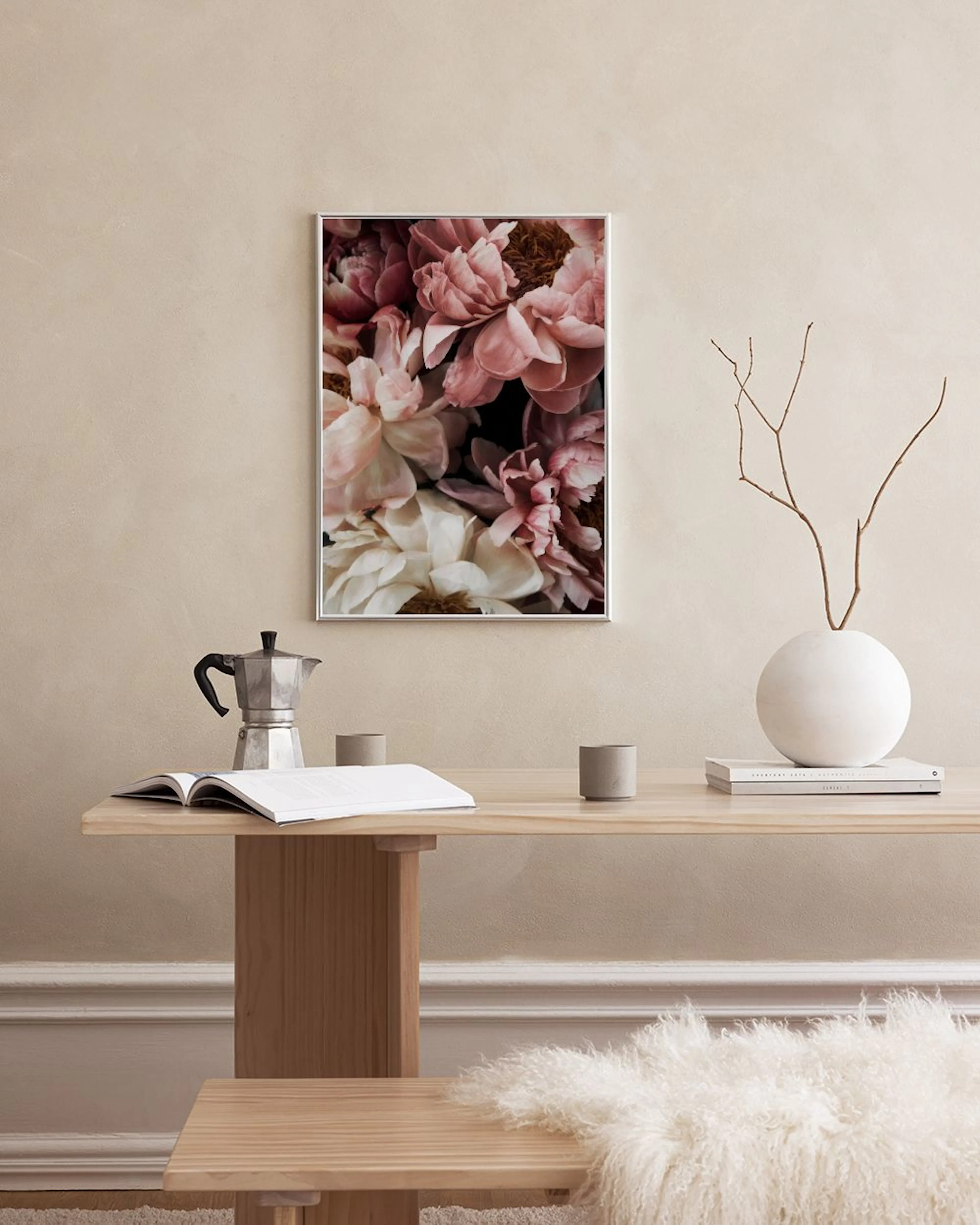 Een poster met roze en witte pioenen, hangend boven een bruin dressoir met vazen en boeken.