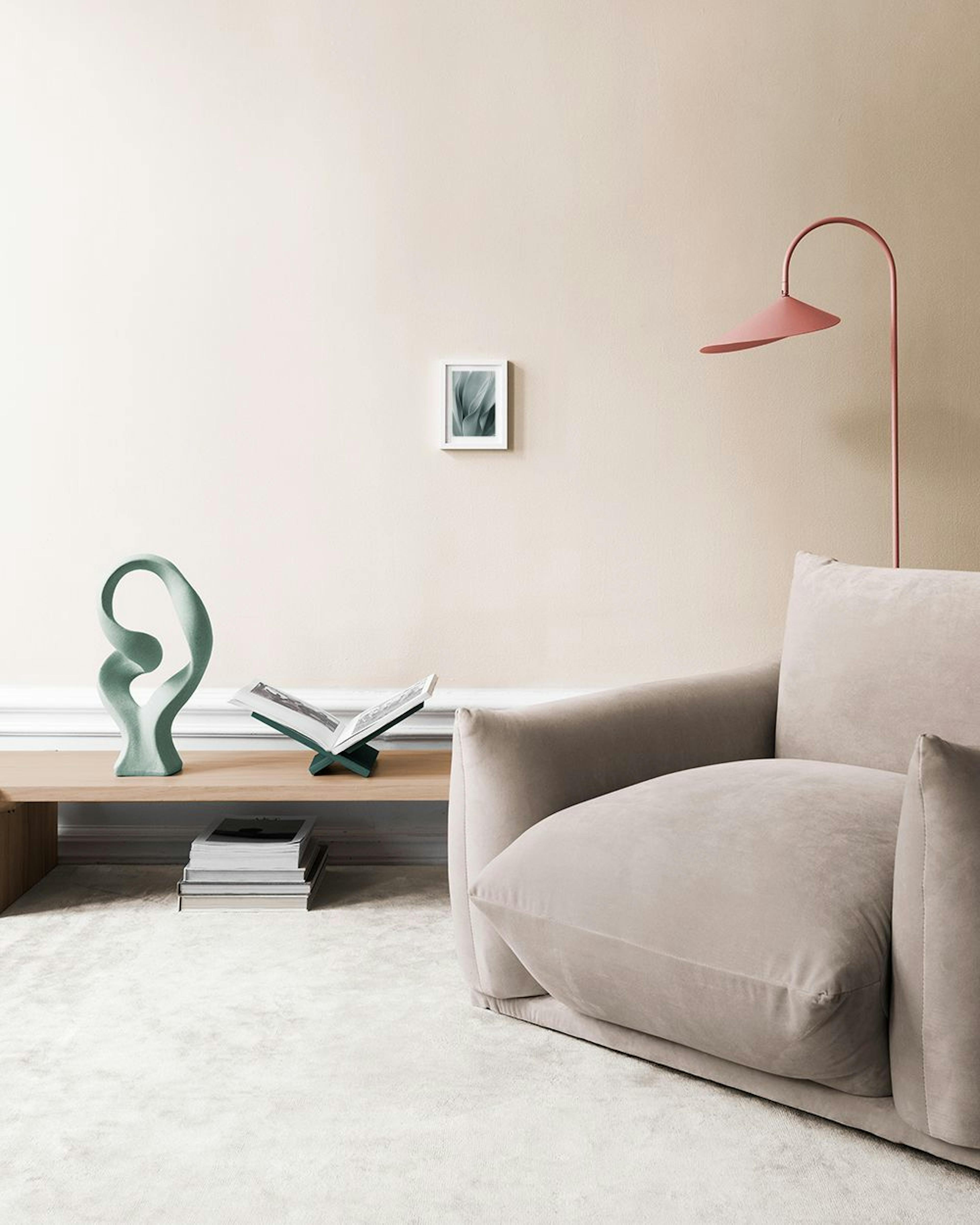 Poster di foglie verde salvia con curve e pieghe, appeso sopra una panca in vimini con libri.