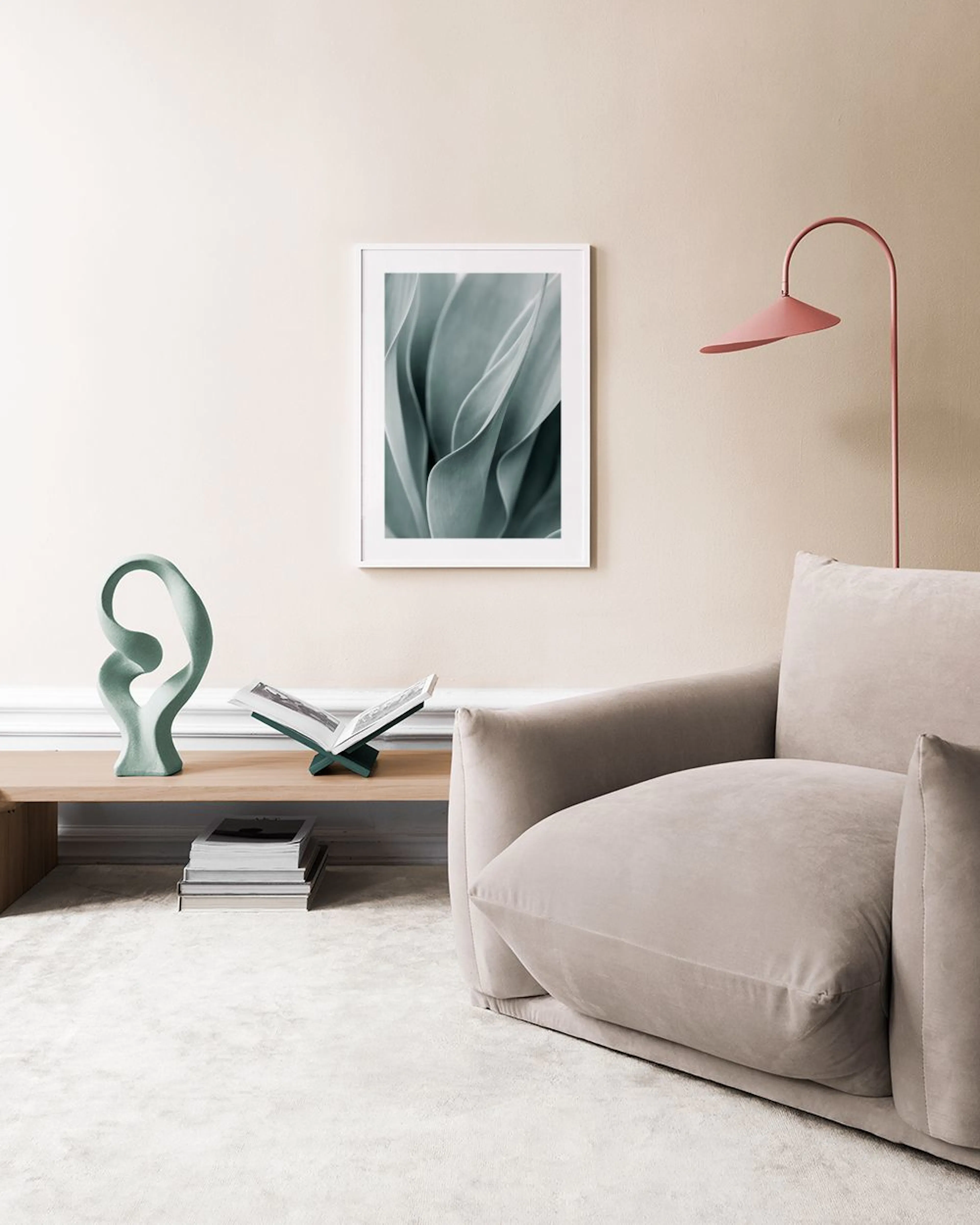 A print of soft green plant leaves with flowing lines, hanging above a natural wood and woven bench with books.