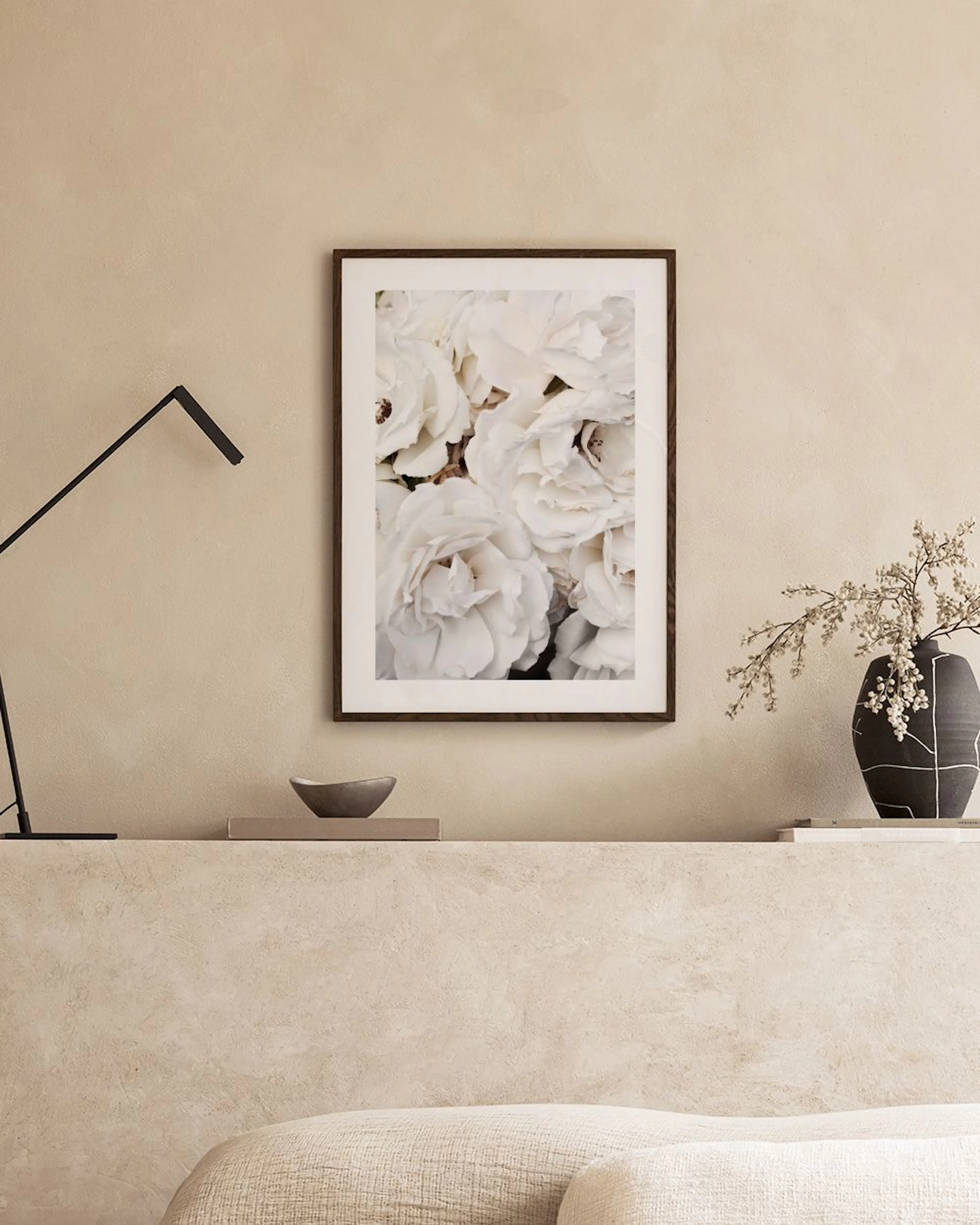Póster de rosas blancas expuesto en una pared gris, con dos candelabros dorados y un puf rosado a un lado.