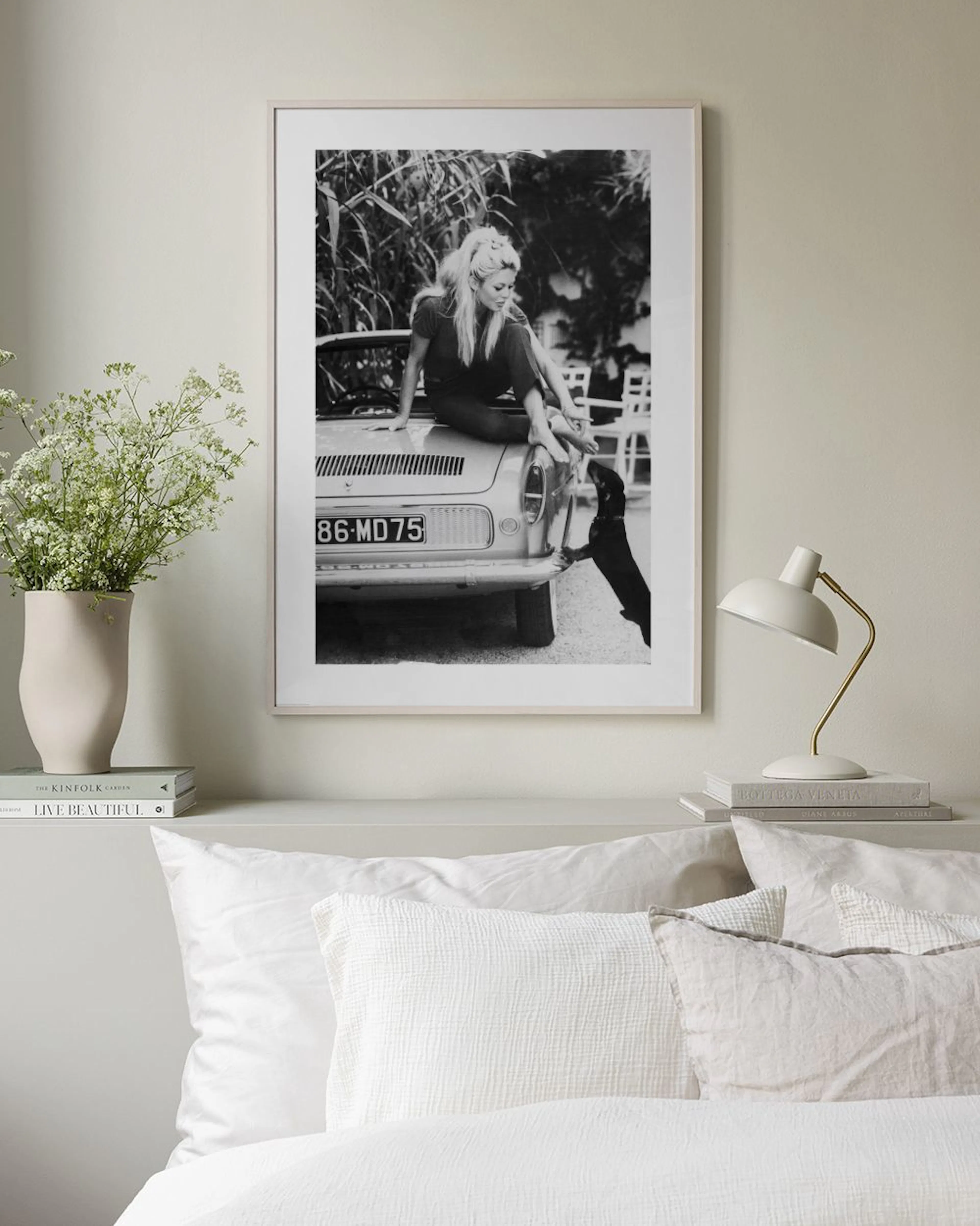 Affiche en noir et blanc de Brigitte Bardot assise sur une voiture, accrochée au mur dans un salon moderne.