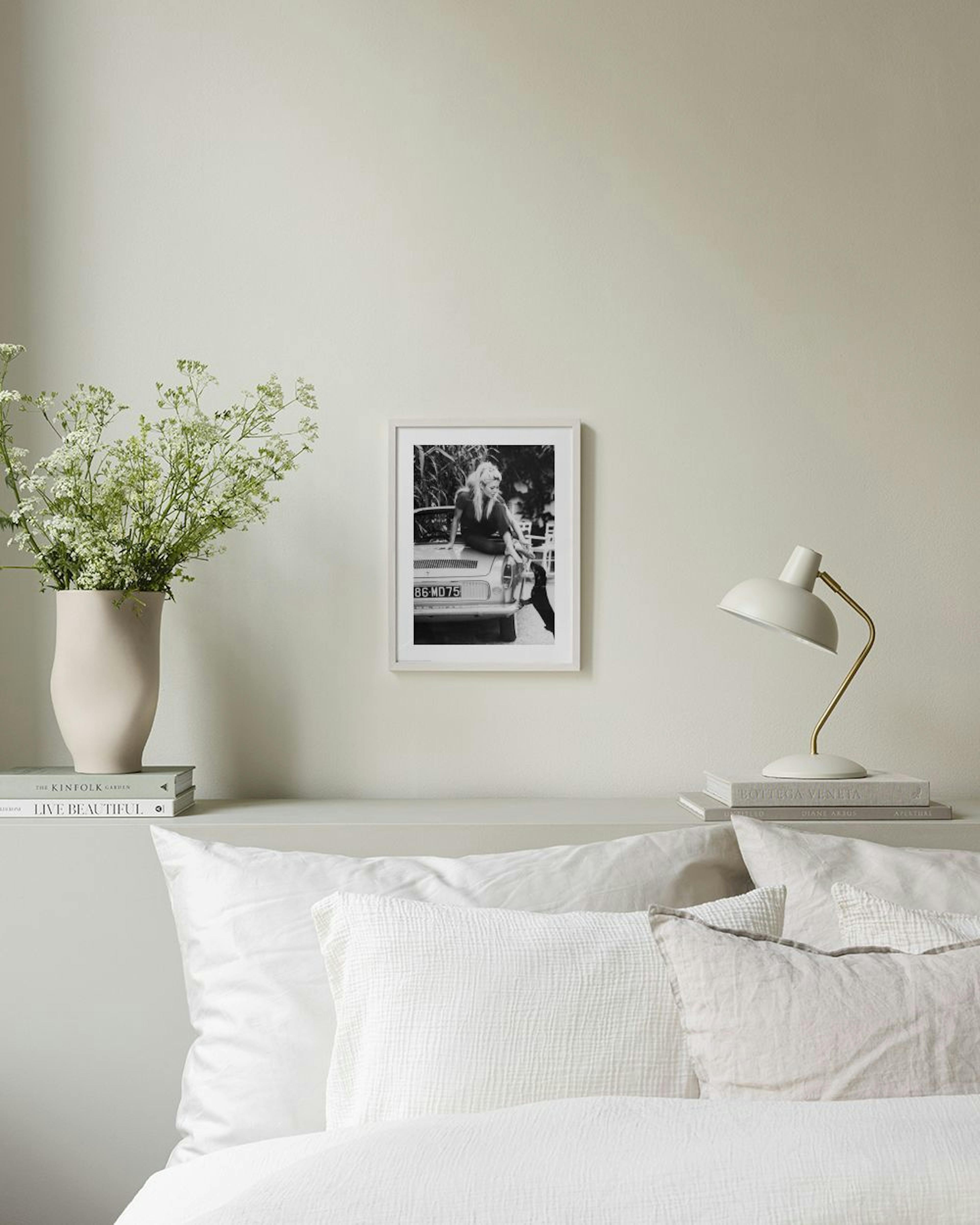 Póster de una mujer rubia sentada en el capó de un coche, en blanco y negro, colgado en una sala de estar moderna.