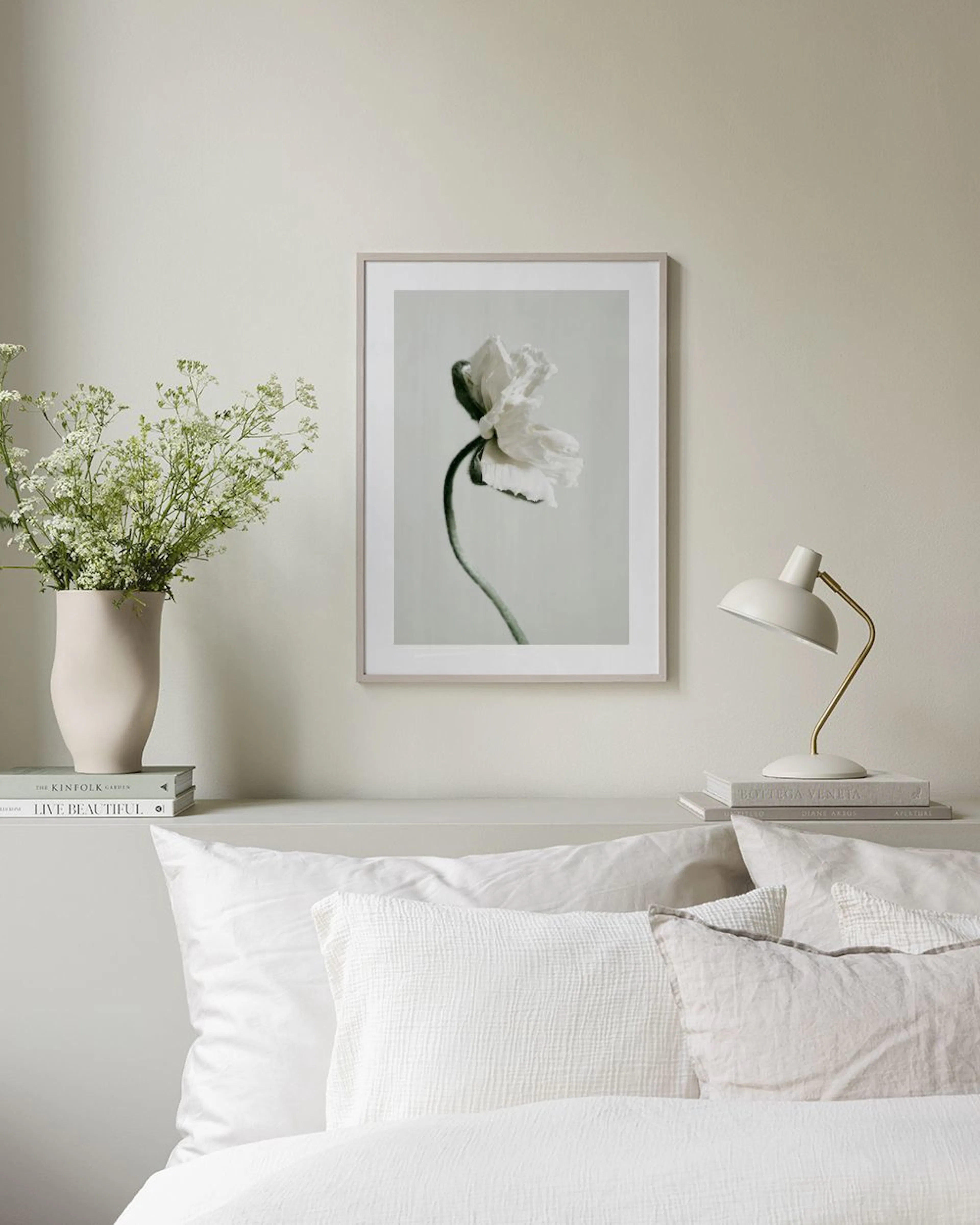 A print of a delicate white poppy with a curved stem on a light background, displayed above a black console table with a dark gr