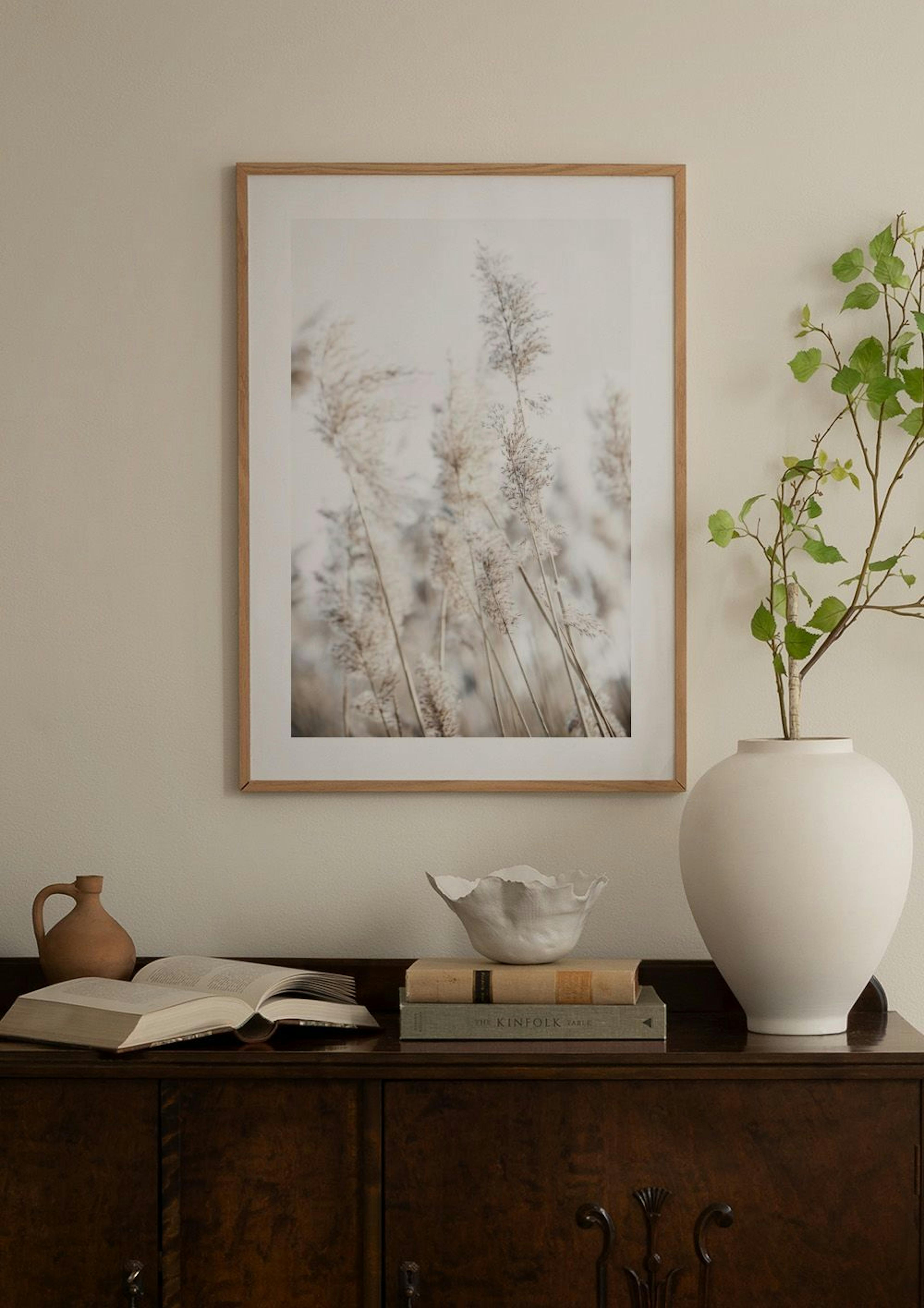 A print of dry pampas grass in light brown and beige tones, hanging on a gray wall above a beige armchair.