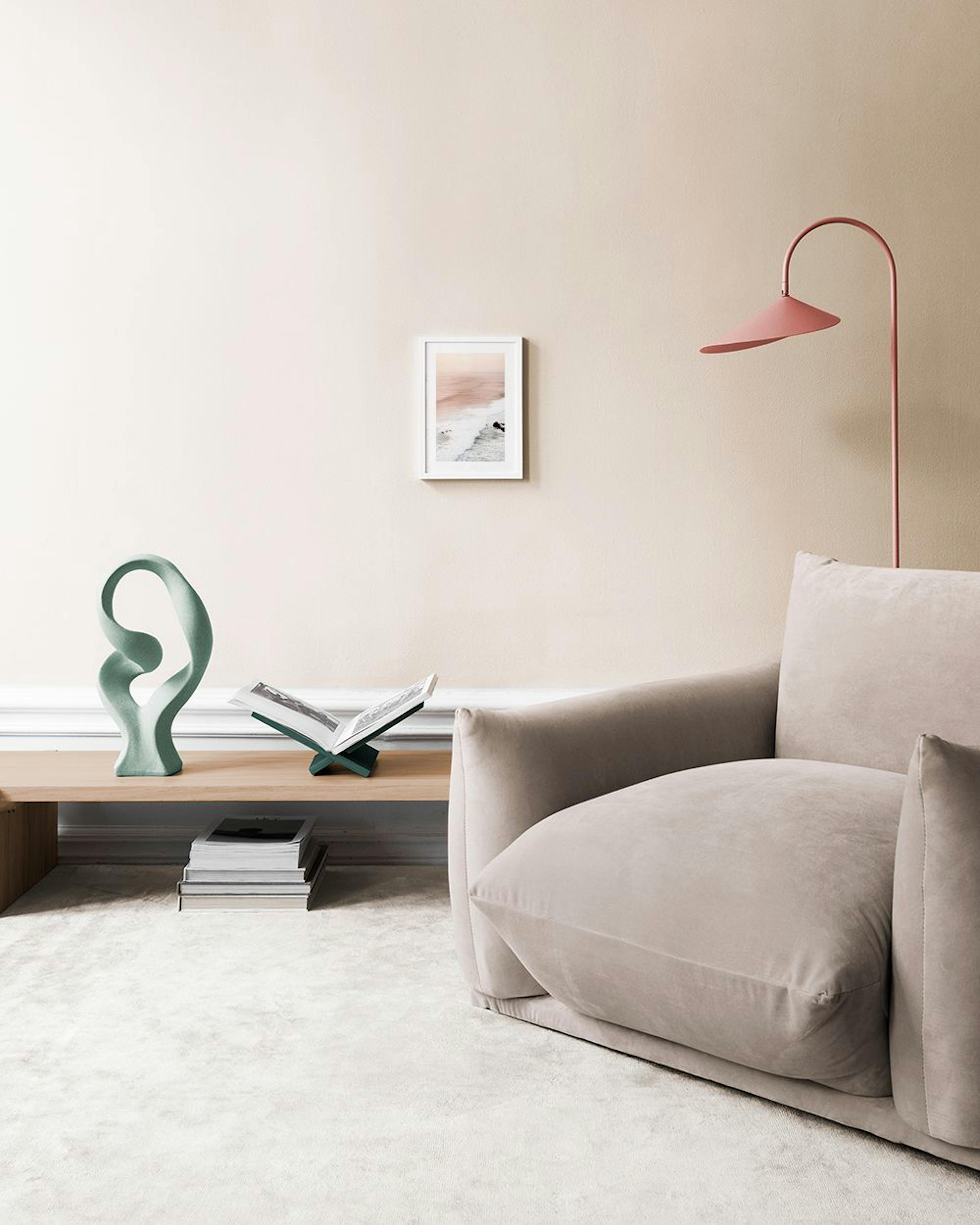 Póster de olas rompiendo en la orilla con cielo rosado, colgado en una sala moderna con silla de terciopelo y mesa auxiliar.
