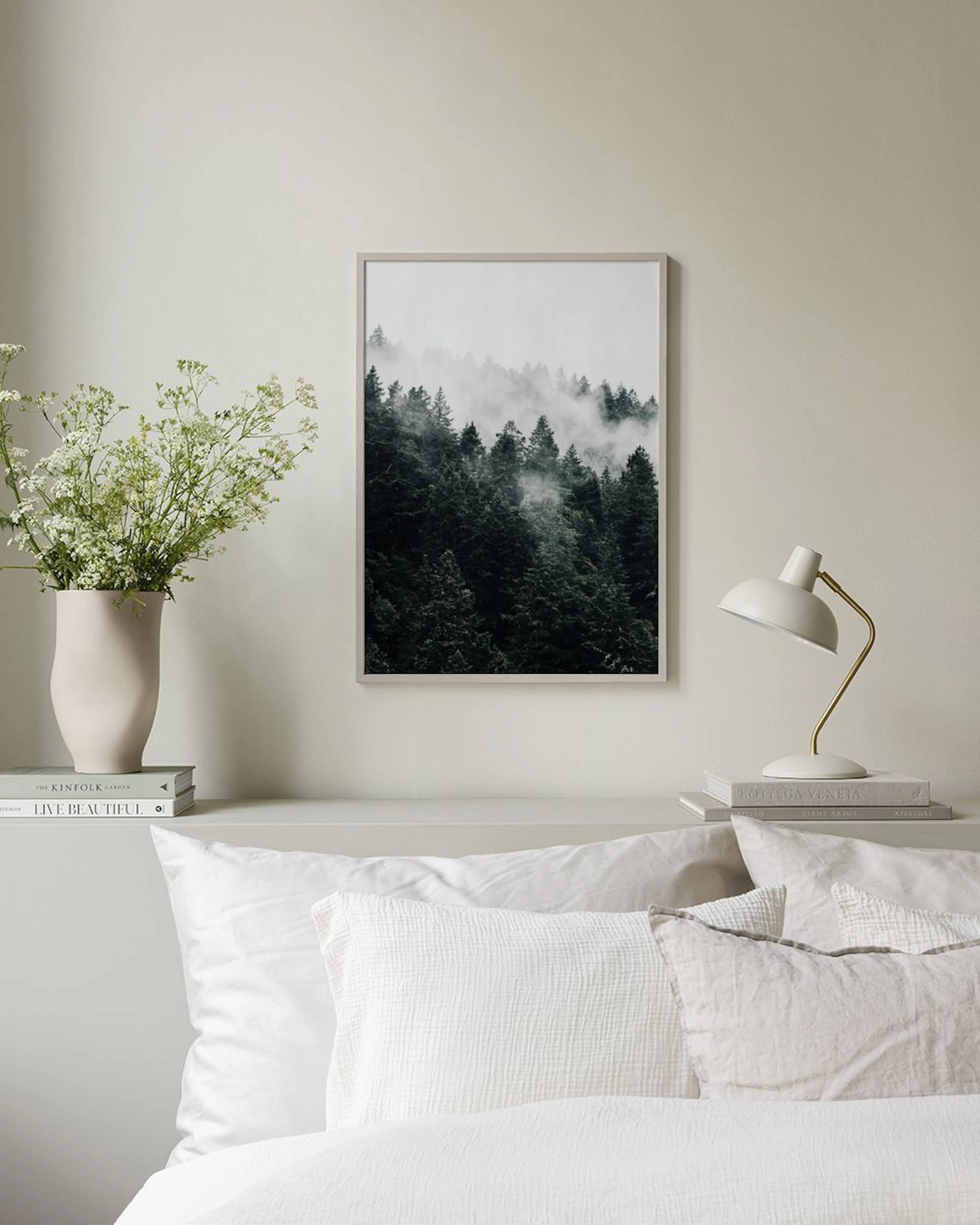 Affiche de forêt brumeuse avec des pins sombres, suspendue dans un salon vert foncé avec pouf et lampe.