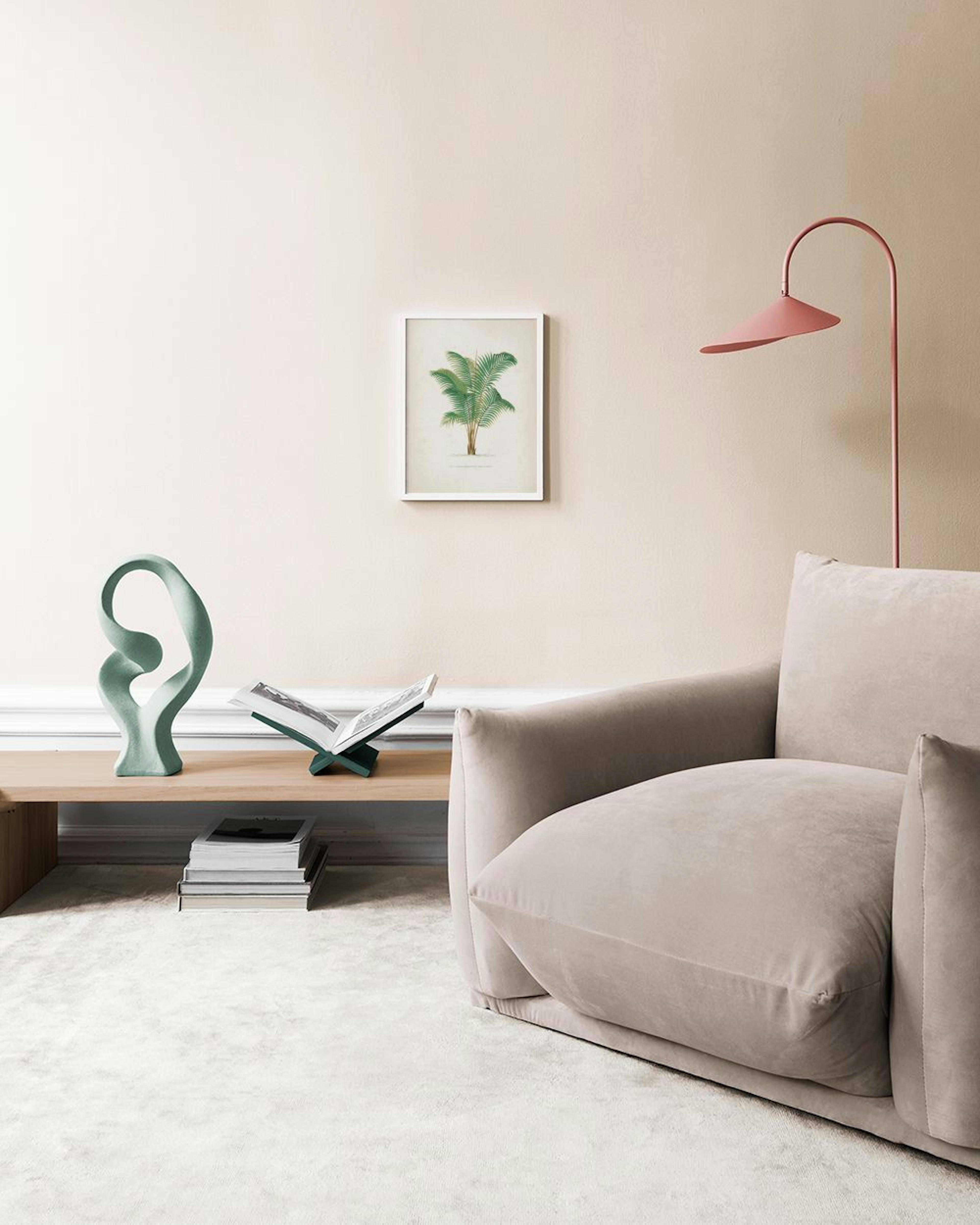 A botanical illustration print of a palm tree, hanging above a dark grey cabinet with a white lamp, books, and decorative object