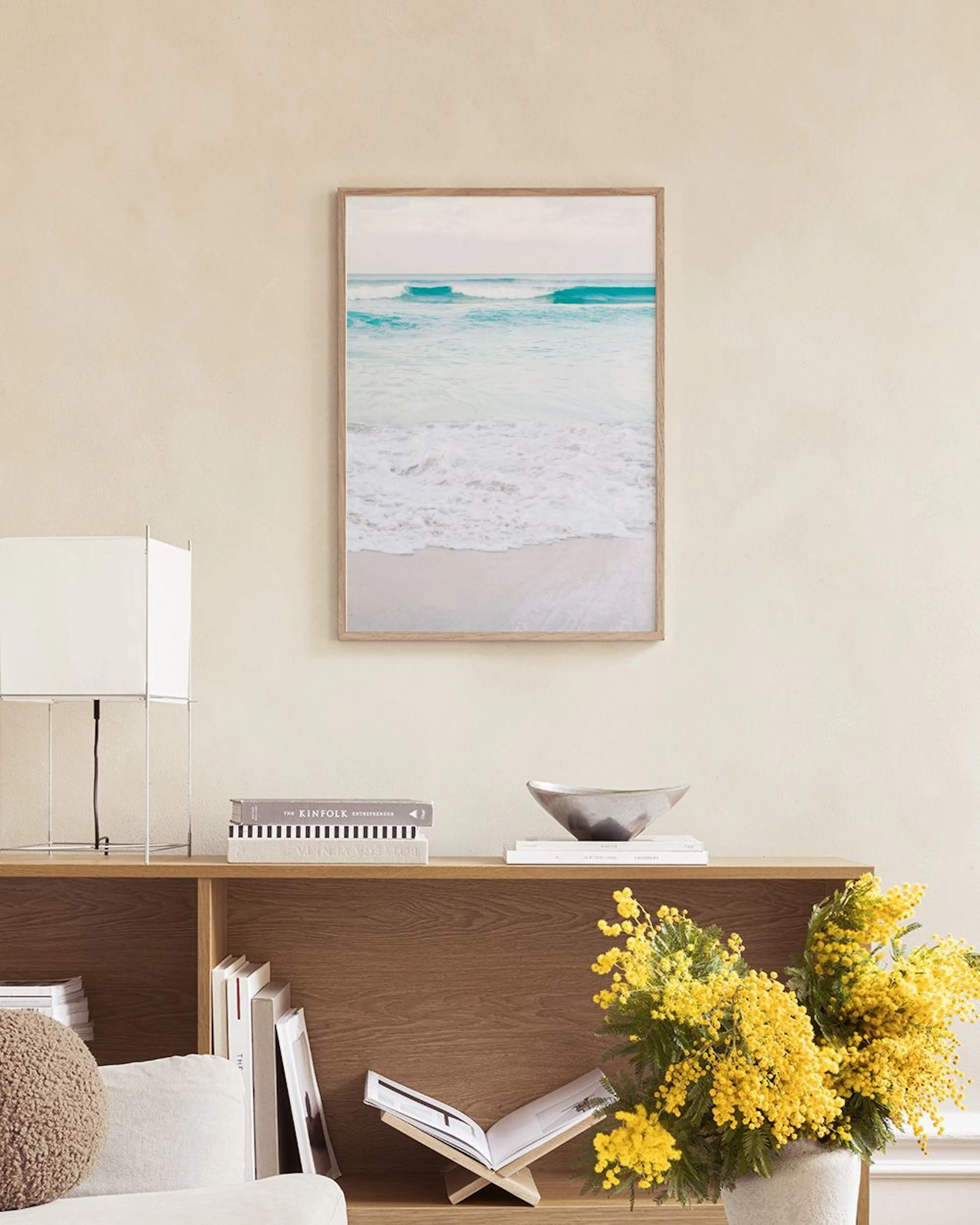 Poster mit Meereswellen am Strand auf einem weissen Sideboard mit Vase und Büchern.