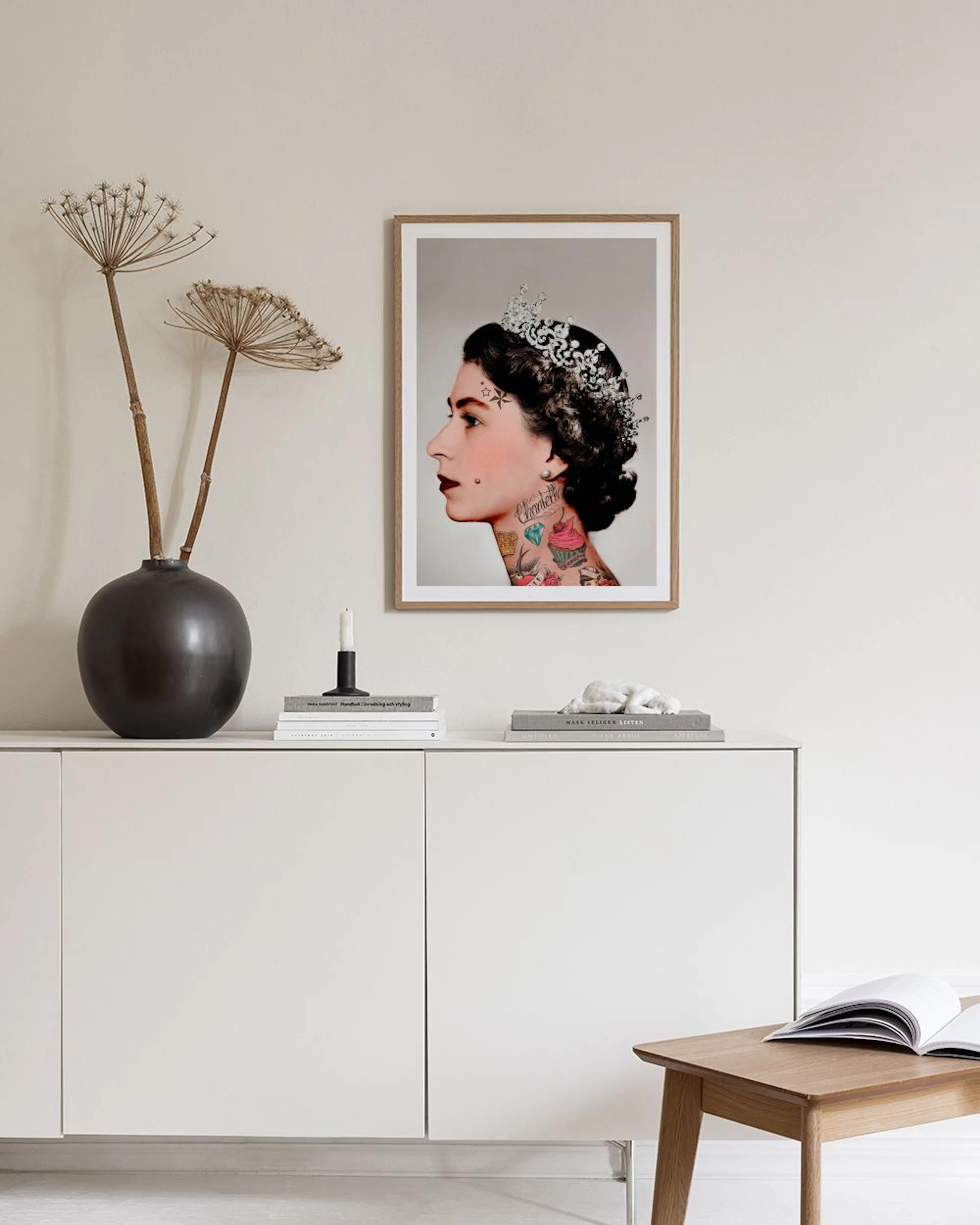 Plakat med punk-inspireret portræt af dronningen i tiara og med tatoveringer, hængende over et mørkeblåt skab i et lyst rum.