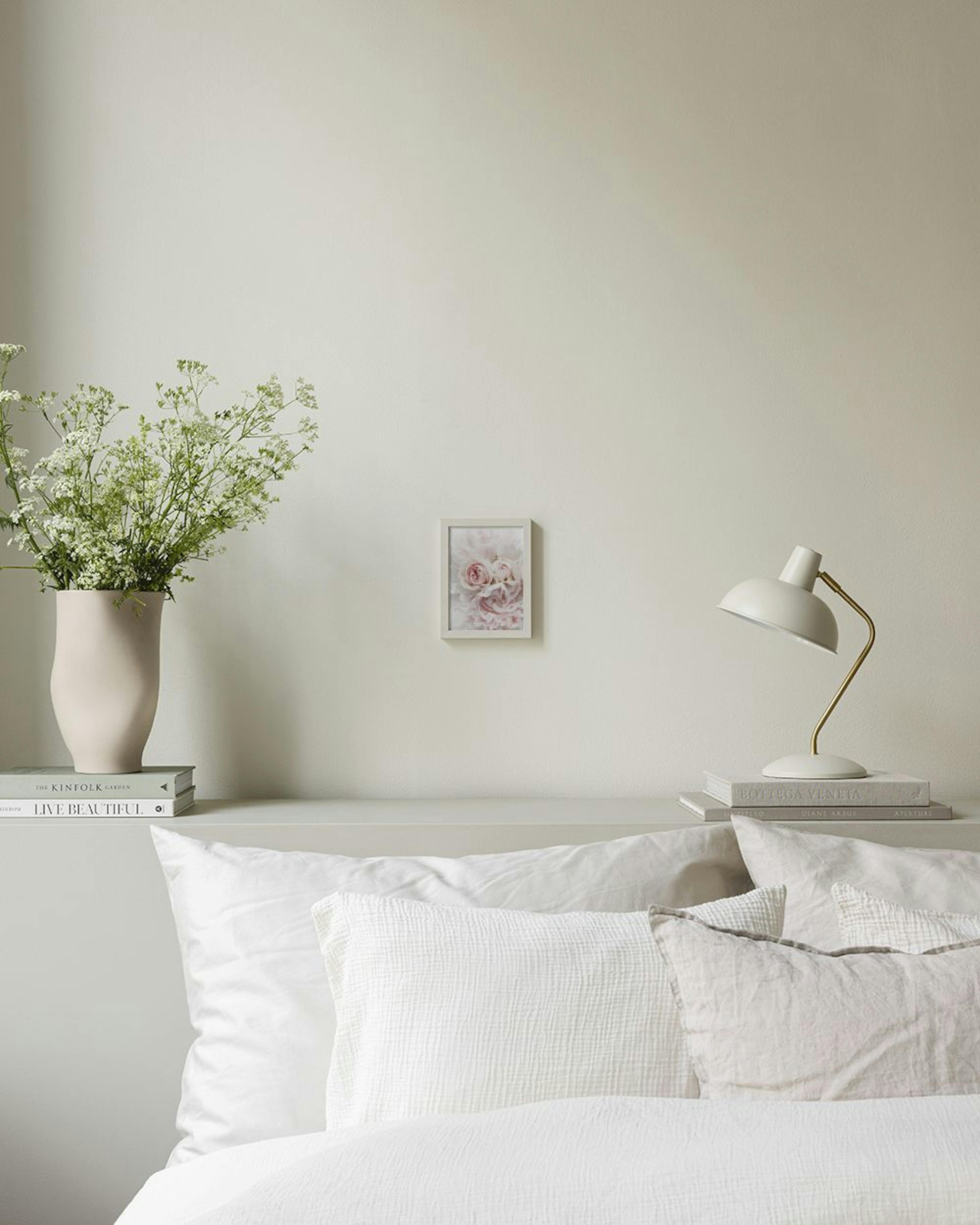 Poster van zachtroze pioenrozen en rozen hangend boven een dressoir met vazen en boeken.