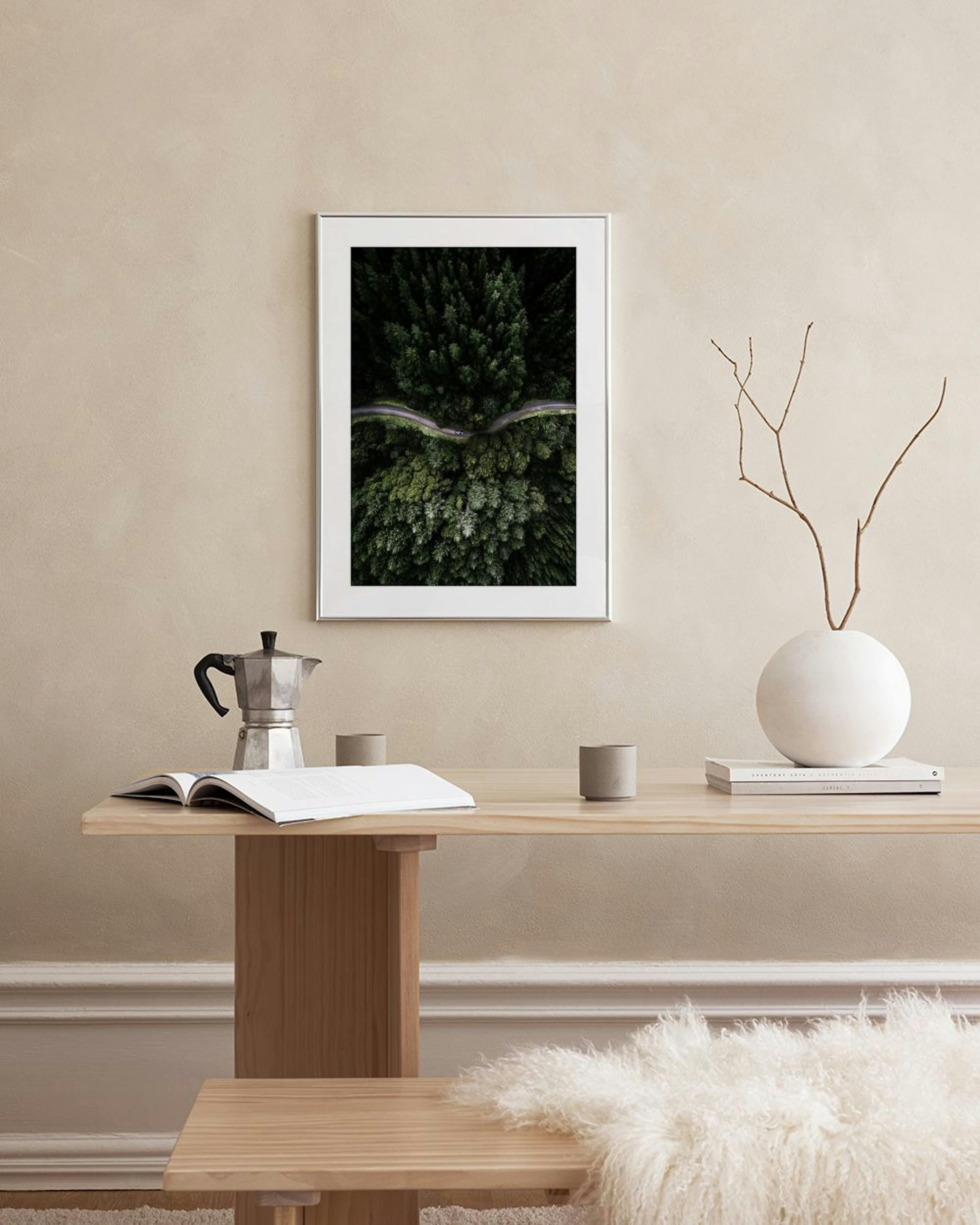 Print of an aerial view of a winding road through a dense green forest, hanging above a white console table in a living room.