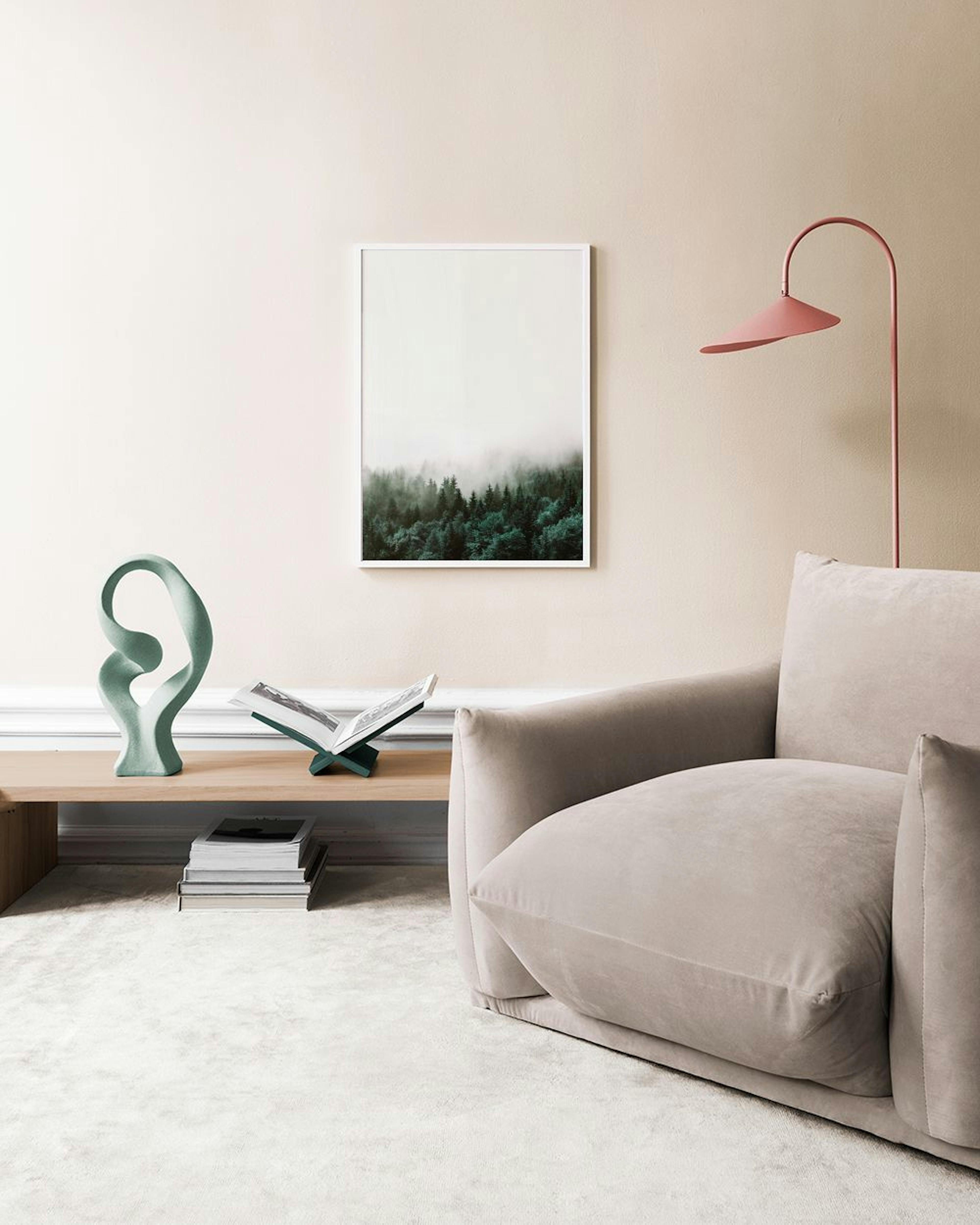 A print of a dark green forest covered in mist, hanging on a black grid wall display in a bright room with a light wood chair an