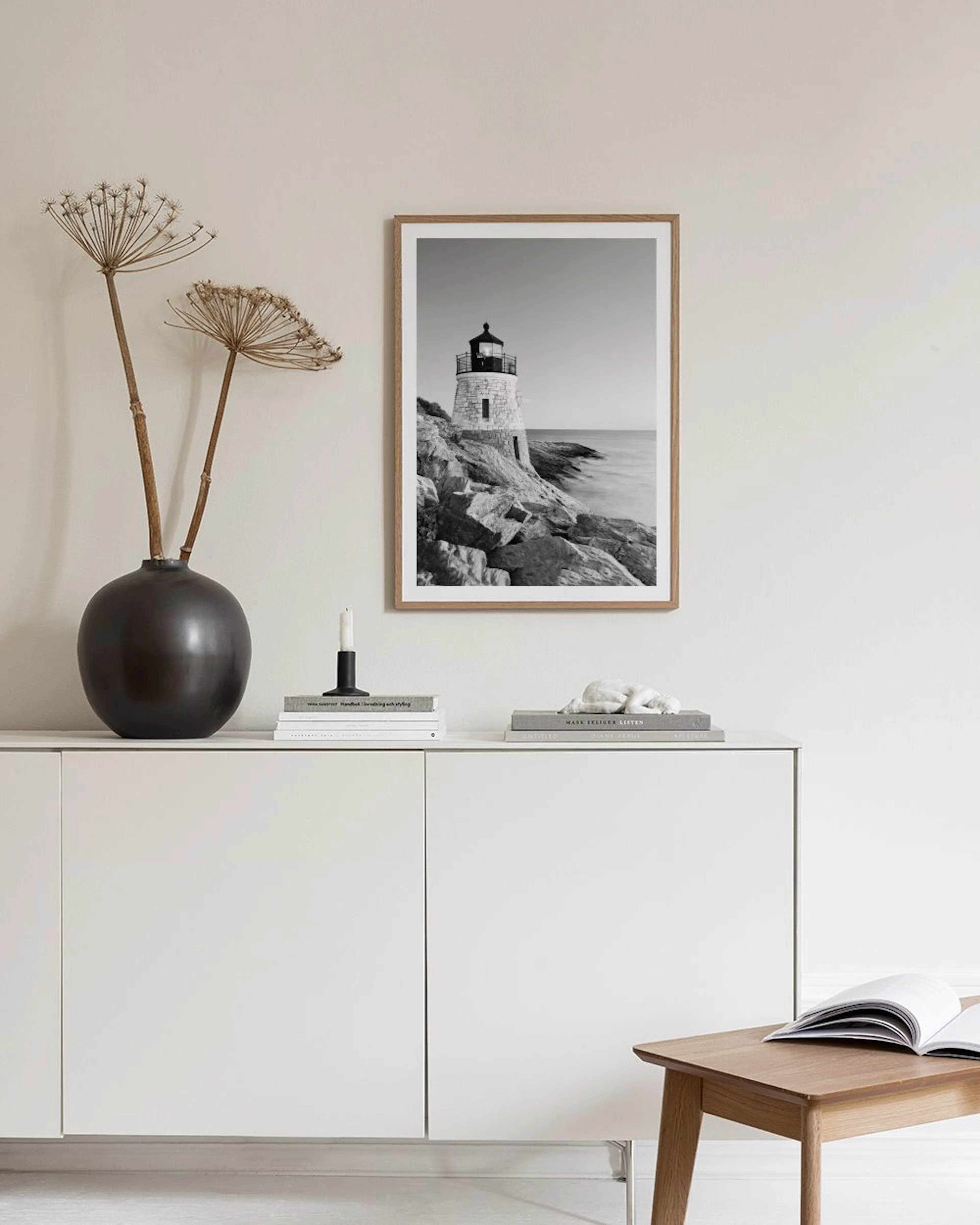 A black and white print of a lighthouse on a rocky coast, displayed on a concrete bench with decorative objects and a lamp.