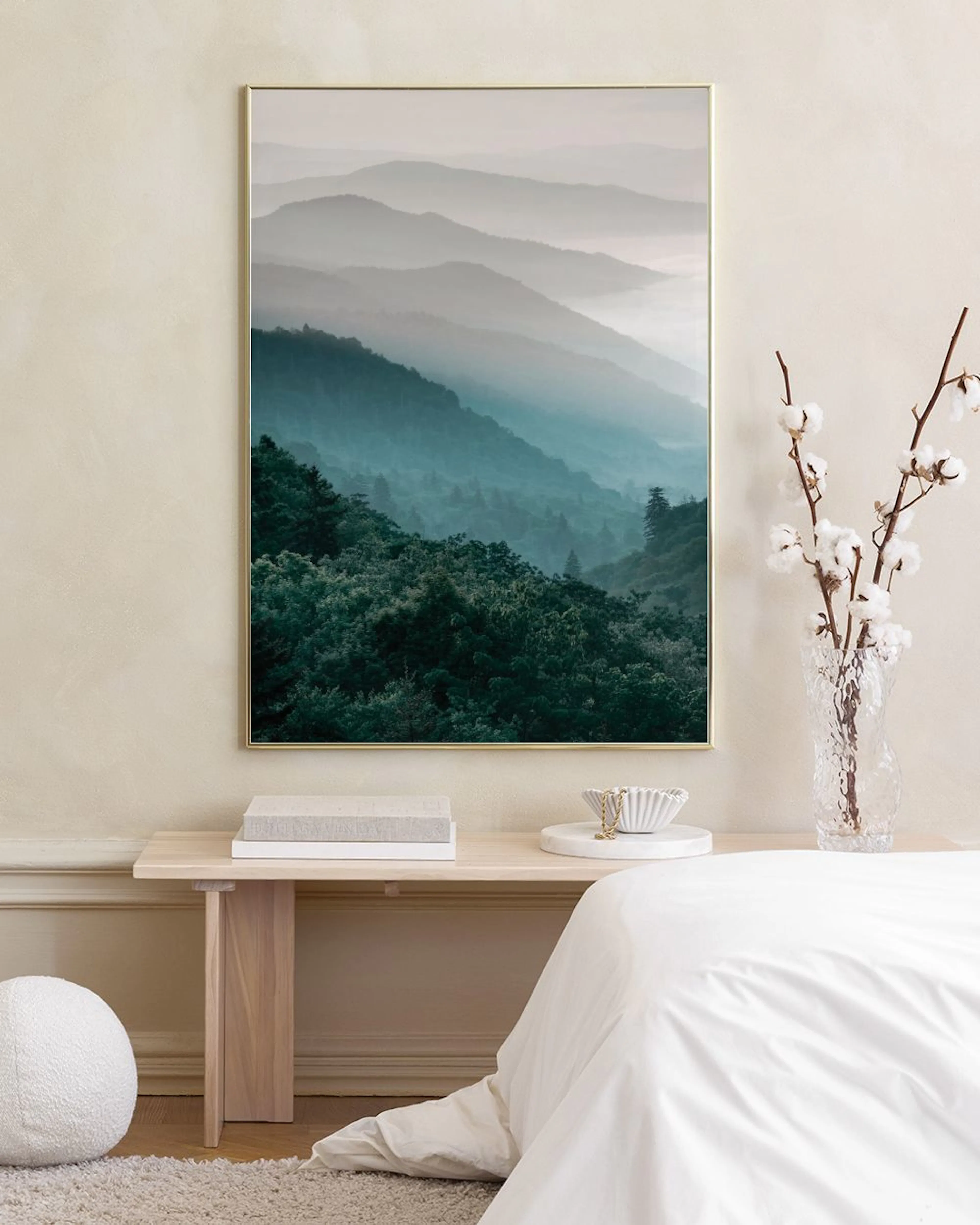 Affiche de montagnes brumeuses aux tons bleus et verts, suspendue au-dessus dun meuble bleu canard avec un vase et une fleur de 