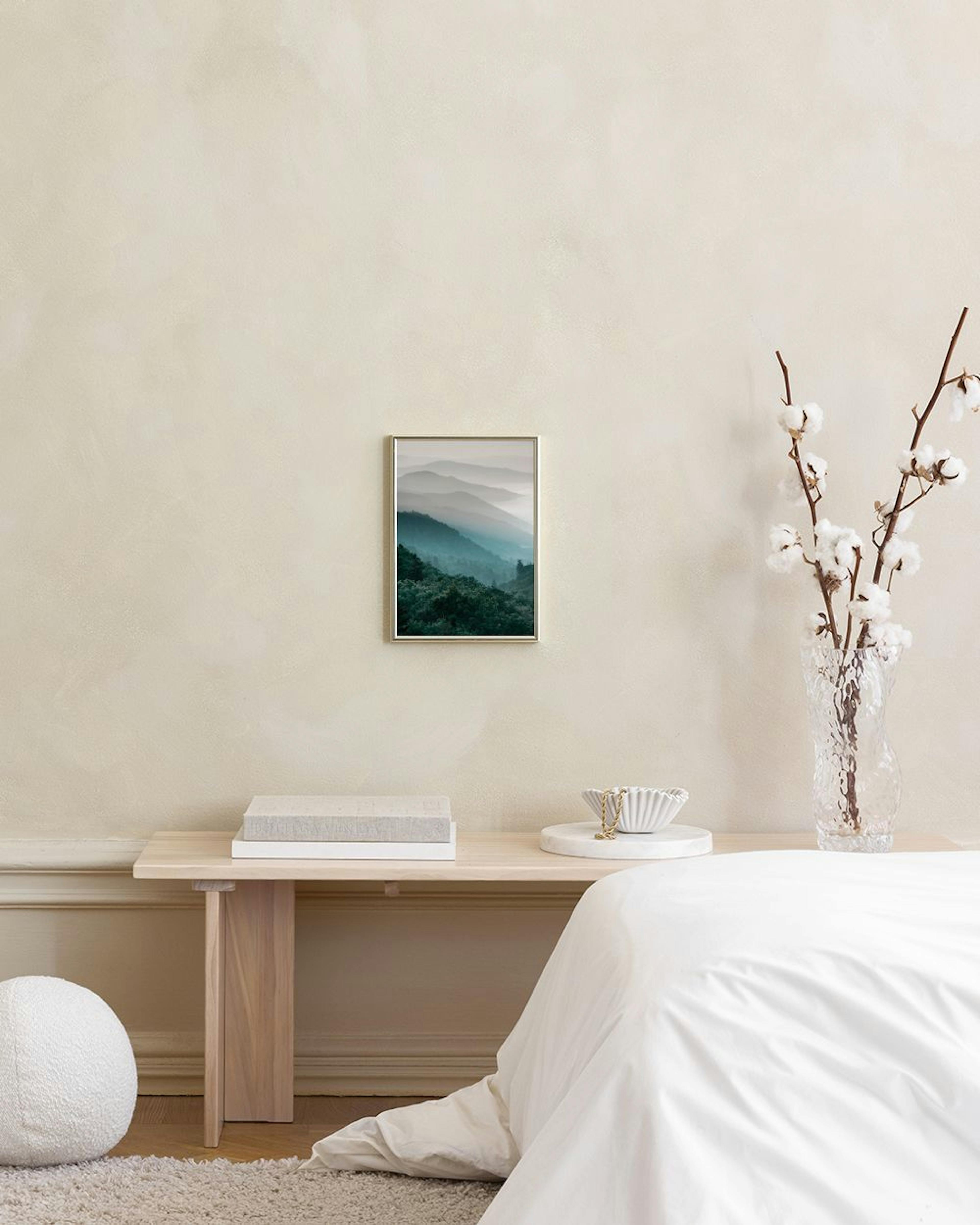 Plakat med tågede bjerge og tæt skov i grønne og blå nuancer, hængende over et blåt skab med en vase og blomster.