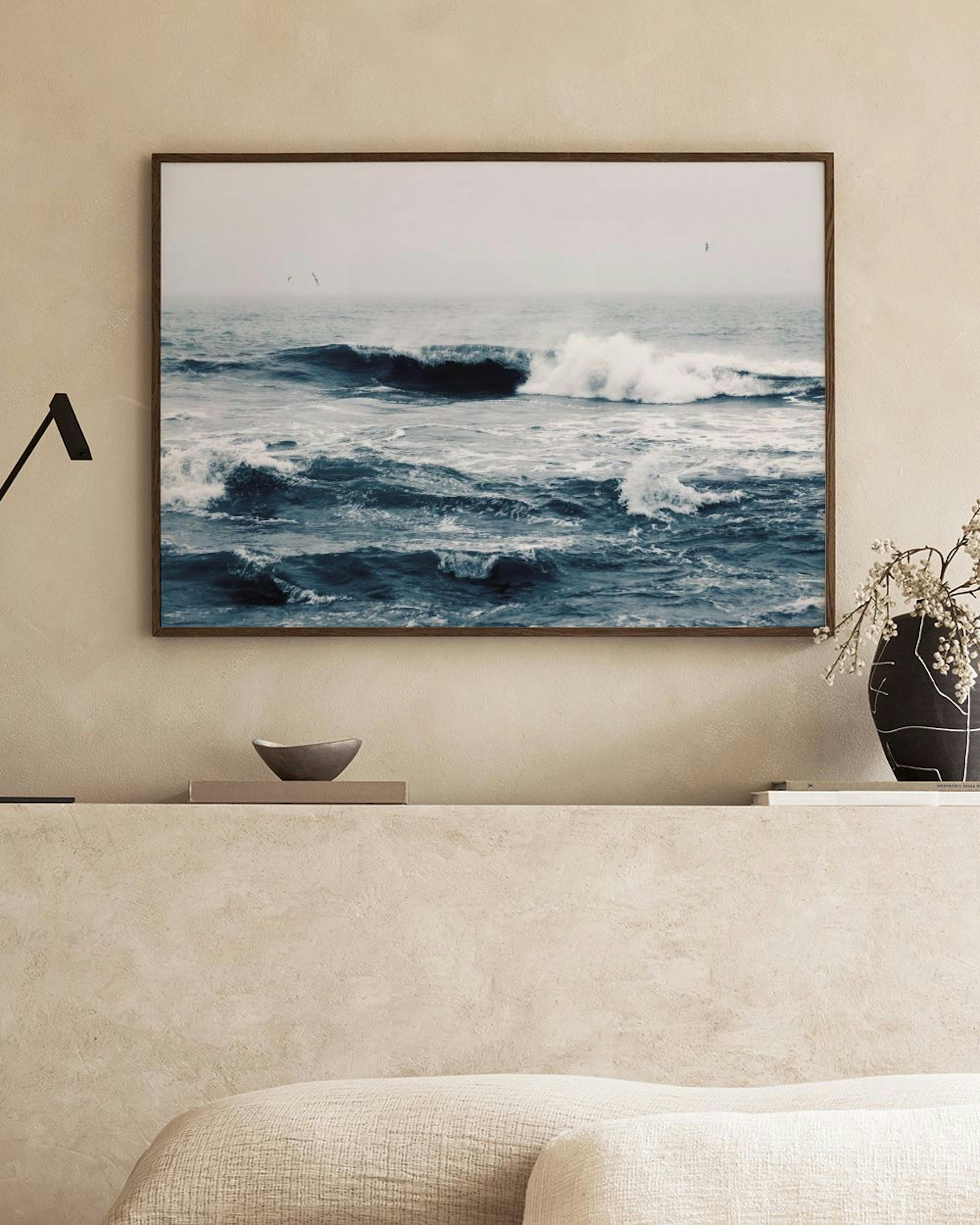 Ocean waves print with a large dark blue wave and white foam, hanging above a light wooden table with glasses.