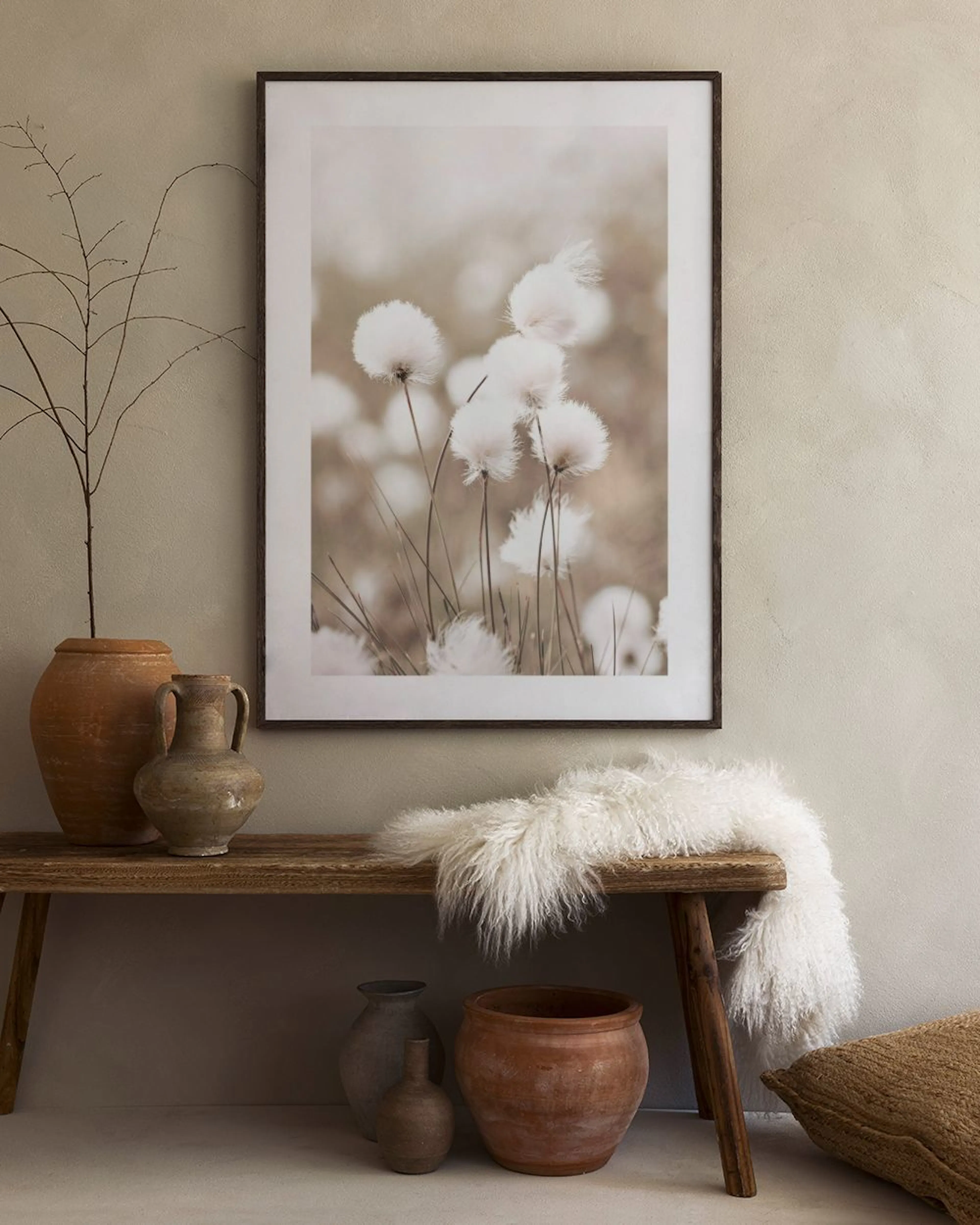A print of delicate white cotton grass flowers on slender stems, displayed above a white modern cabinet with decorative vases an