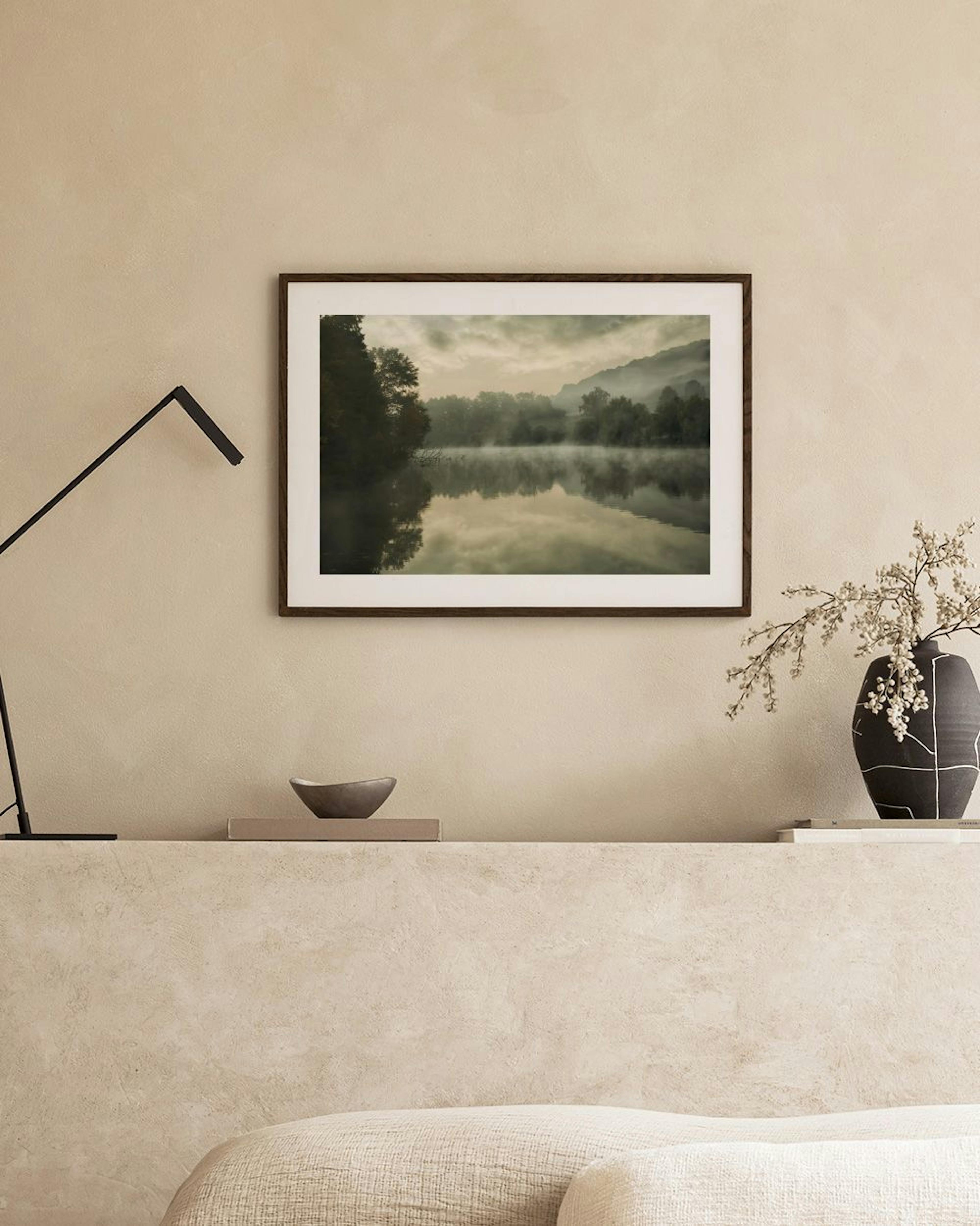 A print of a misty lake surrounded by dark trees and mountains, hanging above a dark wooden cabinet with decorative vases and bo