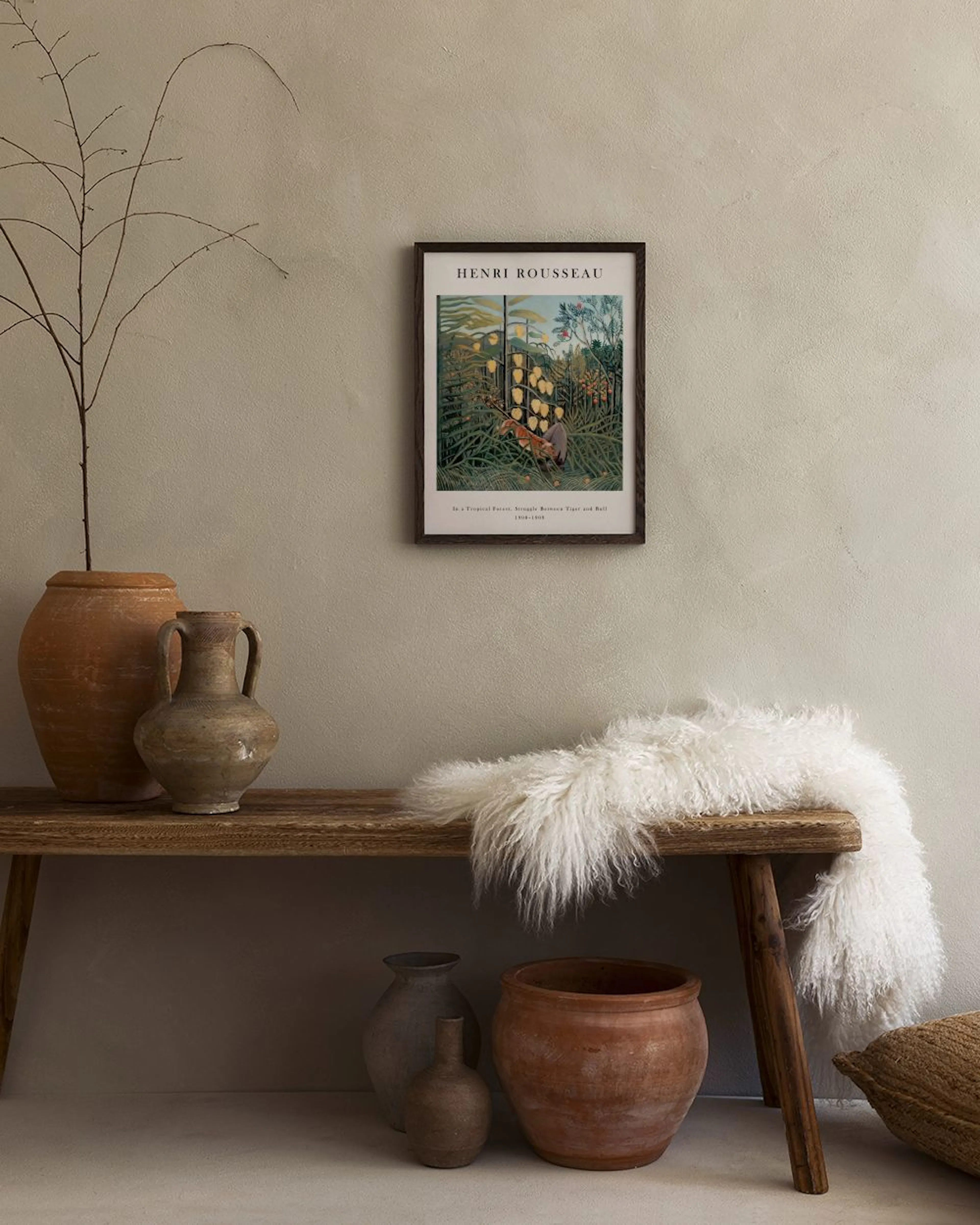 A Henri Rousseau tropical jungle print with a tiger and bull, hanging above a white side table with vases and books.