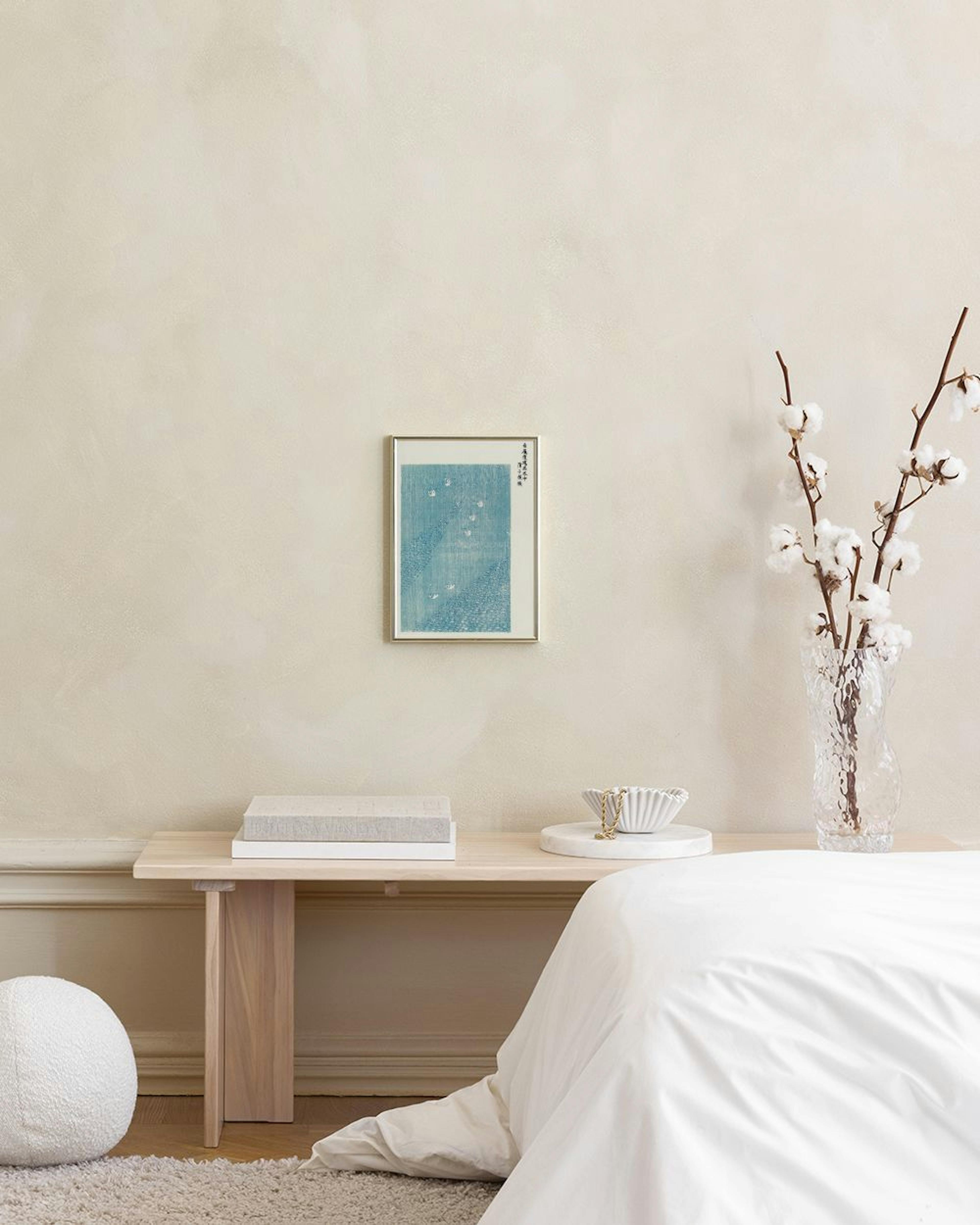A print of a light blue water scene with white floating swans, hanging above a teal cabinet with books and decor.