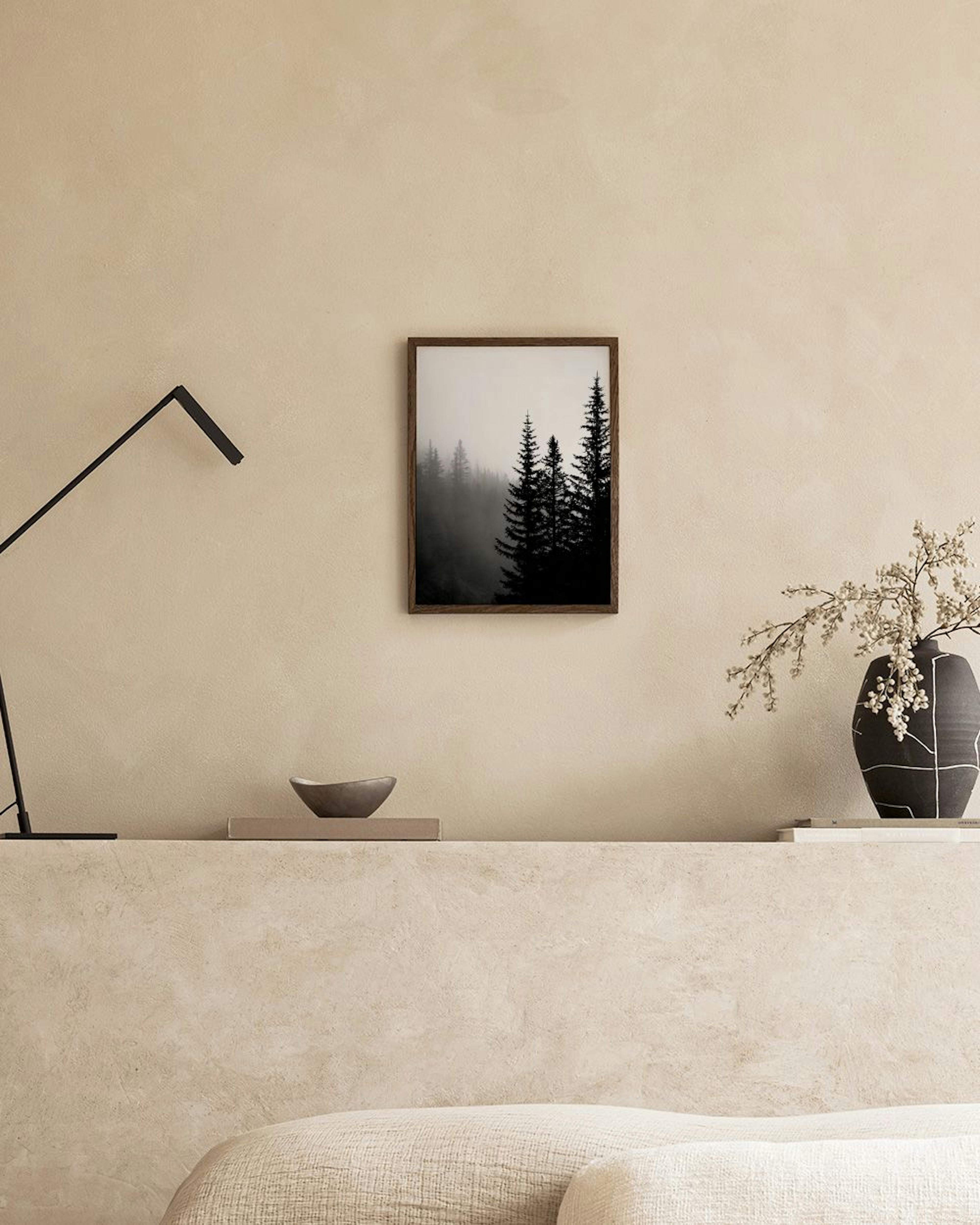 Poster van donkere naaldbomen in mistig bos, hangend boven een wit dressoir met boeken en planten.