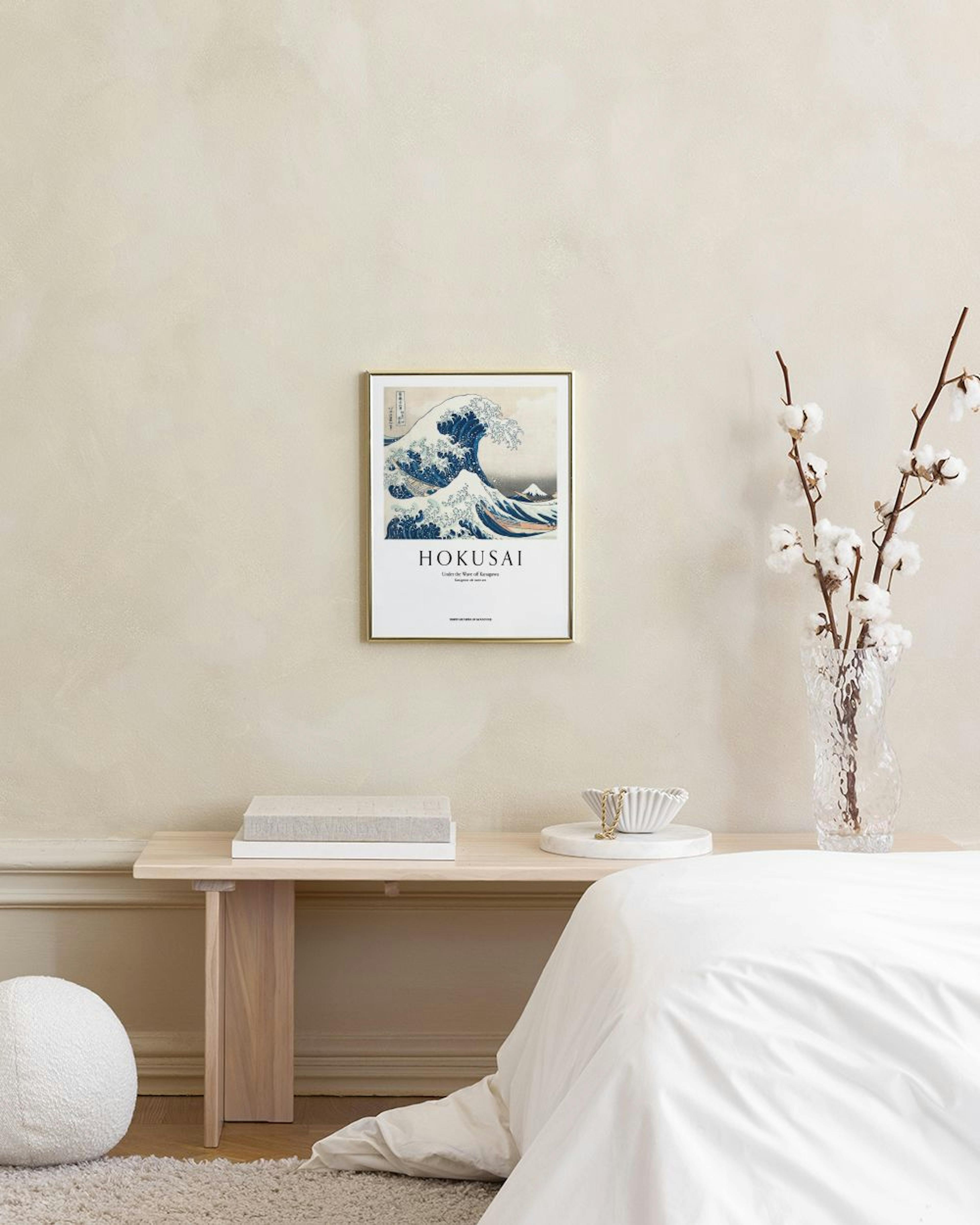 A print of Hokusais The Great Wave off Kanagawa hangs on a grey wall above a light grey table and blue ottoman.