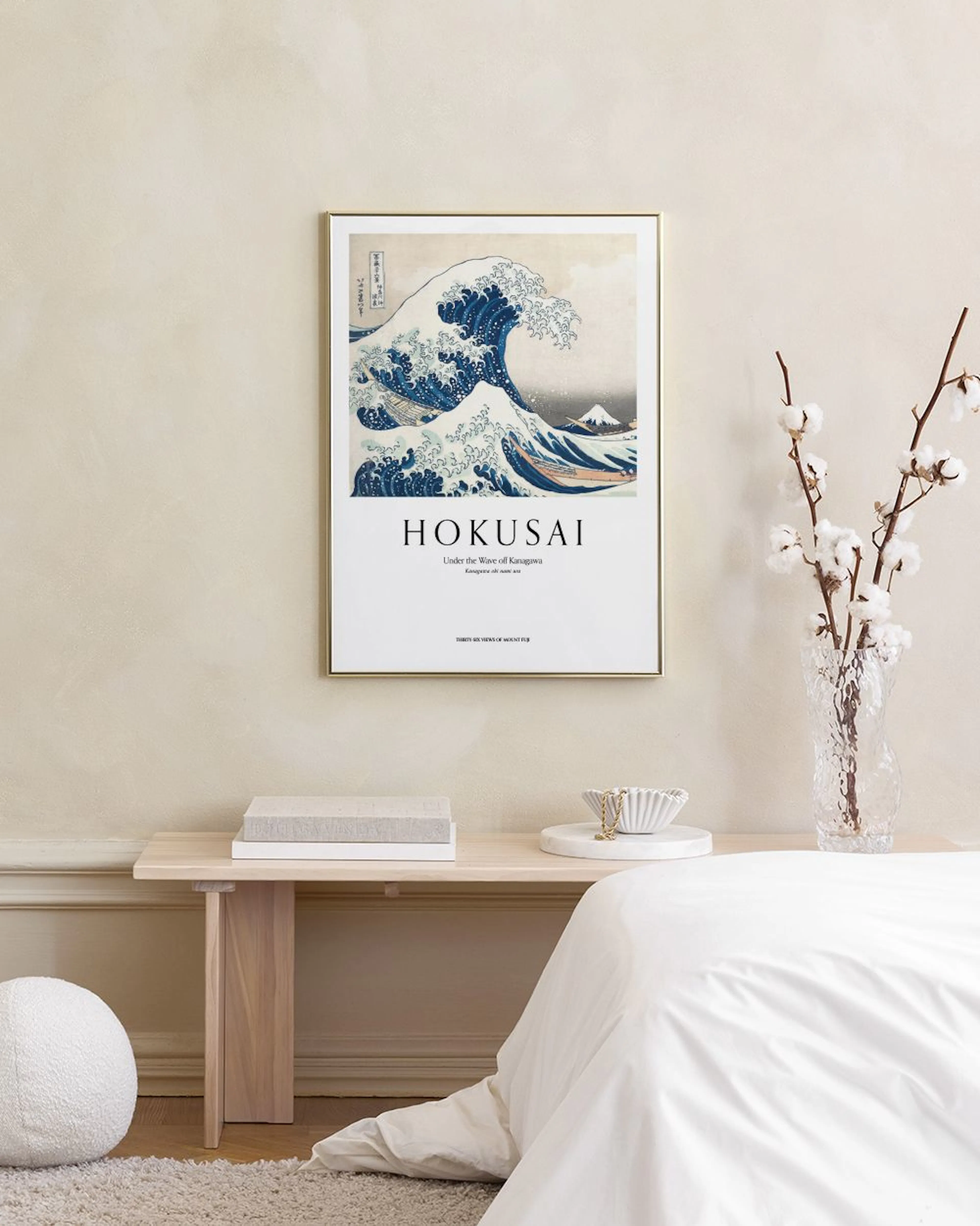 A print of Hokusais The Great Wave off Kanagawa hangs on a grey wall above a light grey table and blue ottoman.