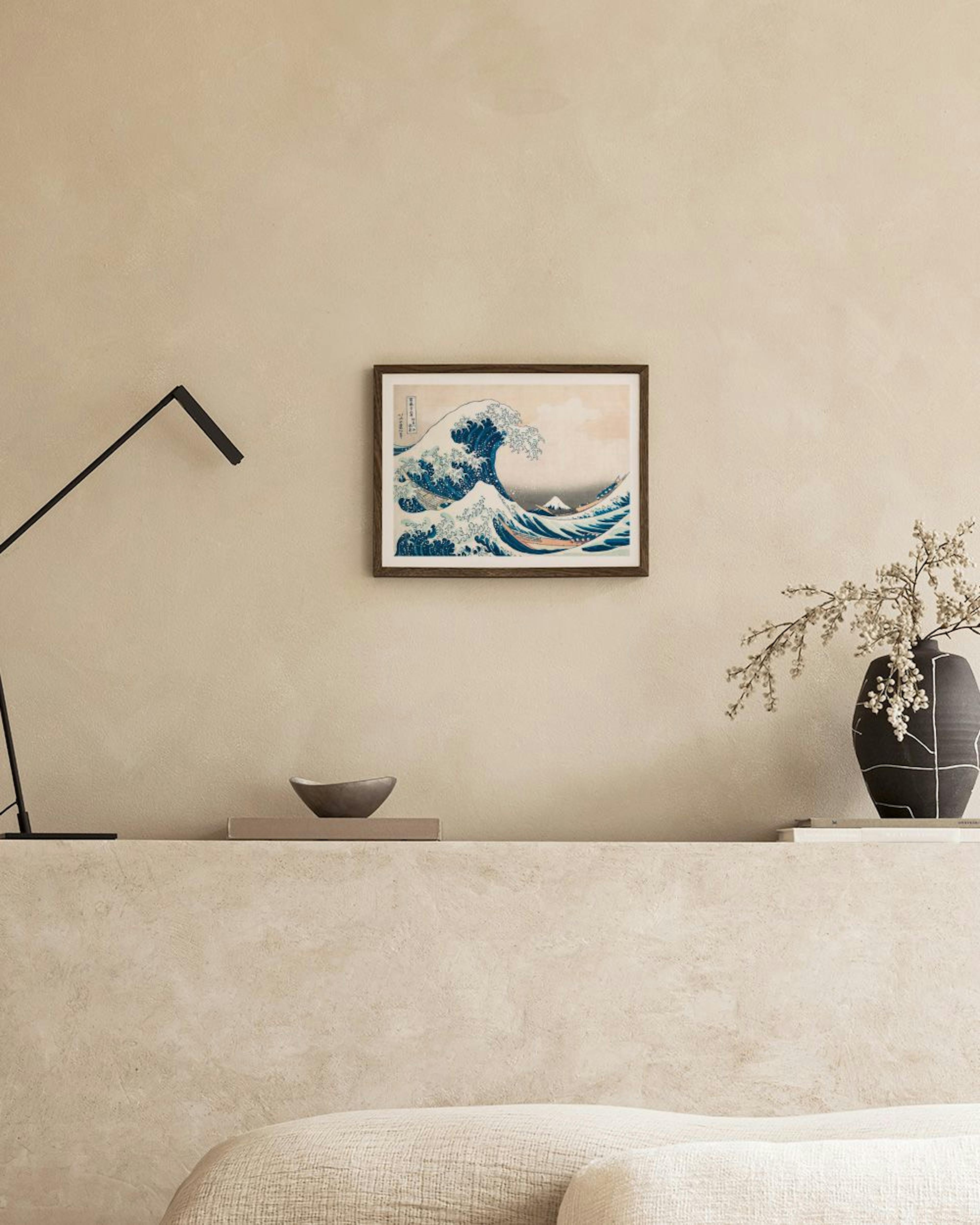 Poster med Hokusais Den stora vågen, hängandes på en ljusgrå vägg ovanför ett sidobord med runda dekorationer och en stol.