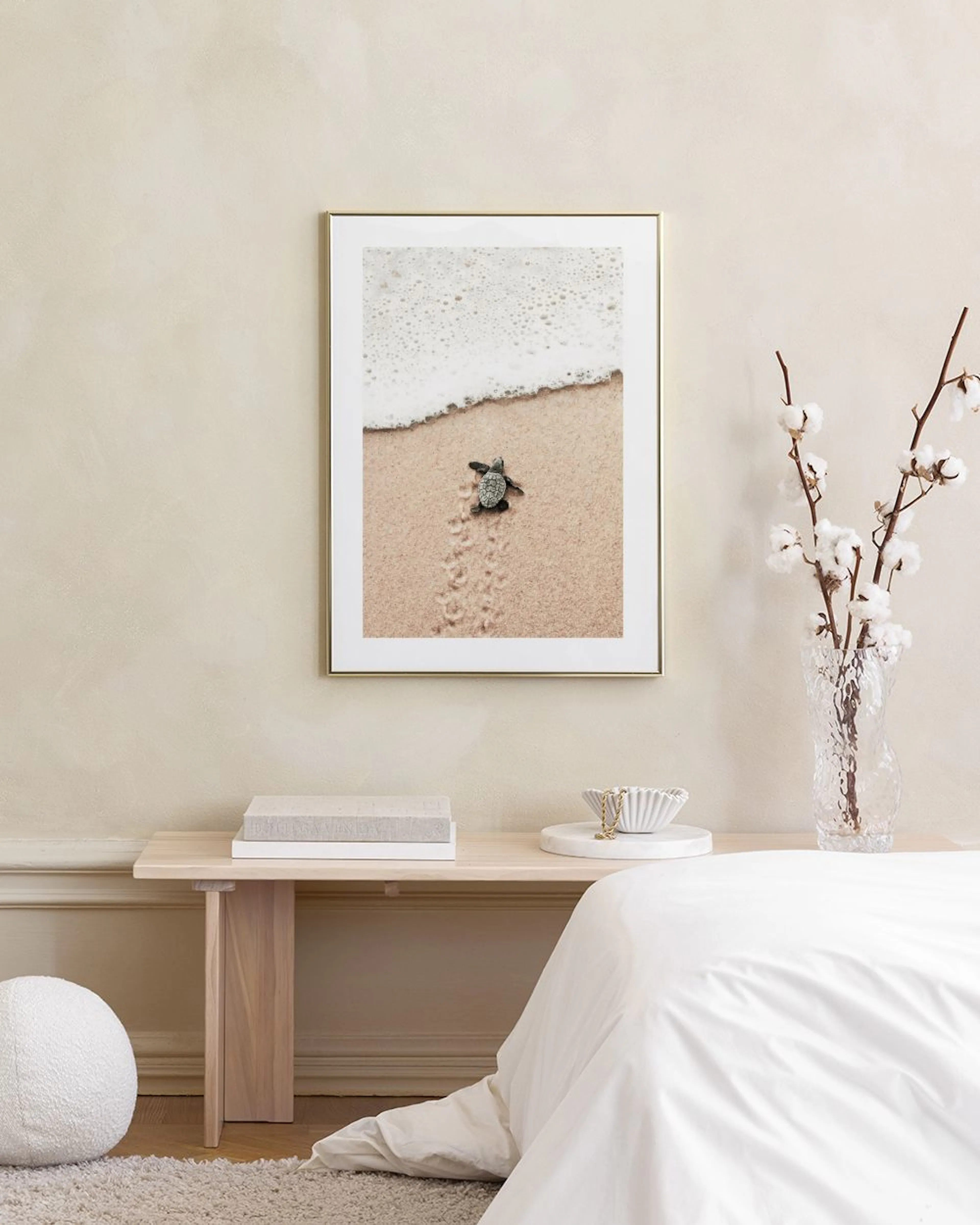 Plakat med en havskildpaddeunge på vej mod havet fra sandstranden, ophængt i et lyst, minimalistisk rum over en hvid skænk.