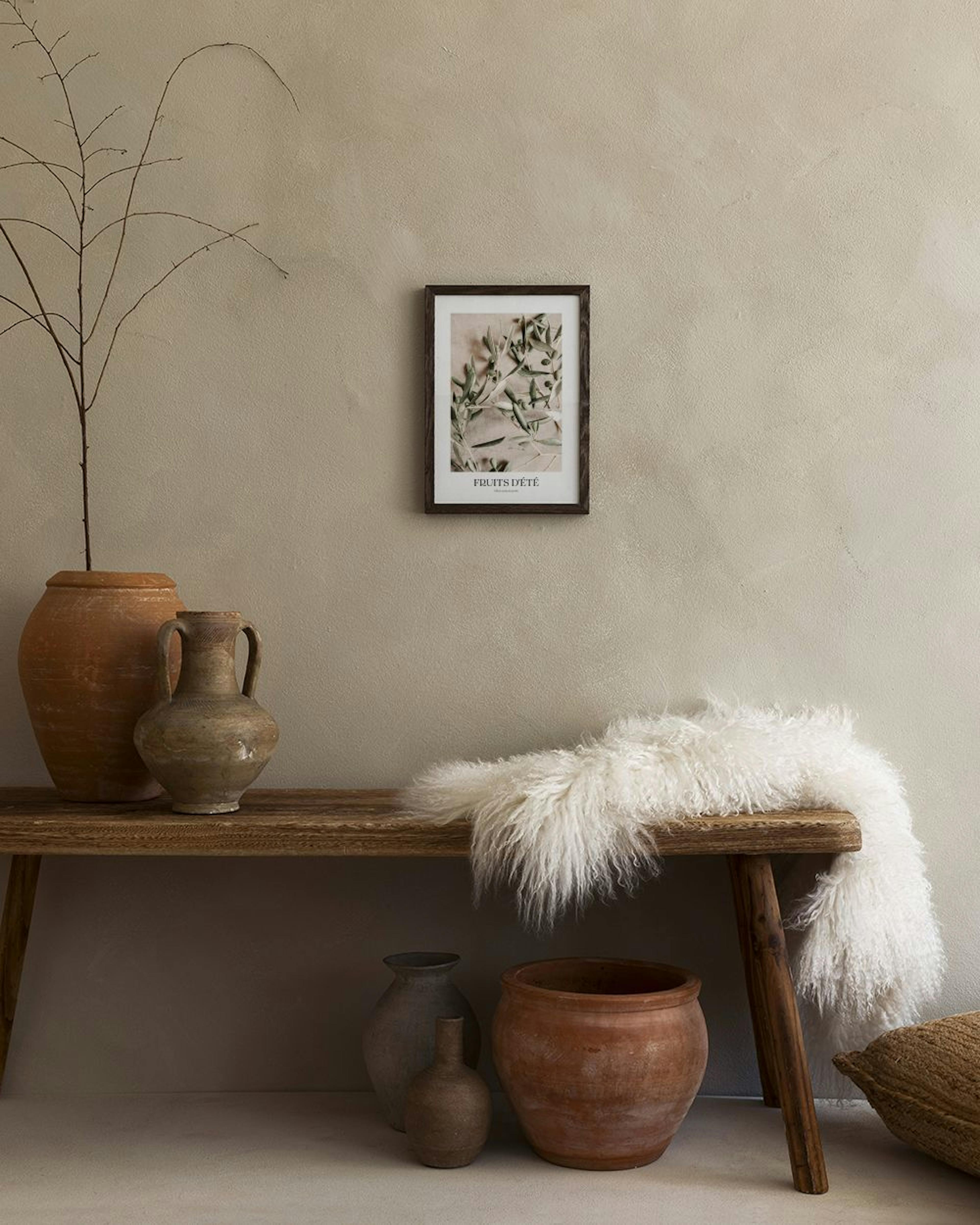 Poster met olijftakken en kleine olijven op een beige achtergrond, staand op een grijze sidetable in een modern interieur.