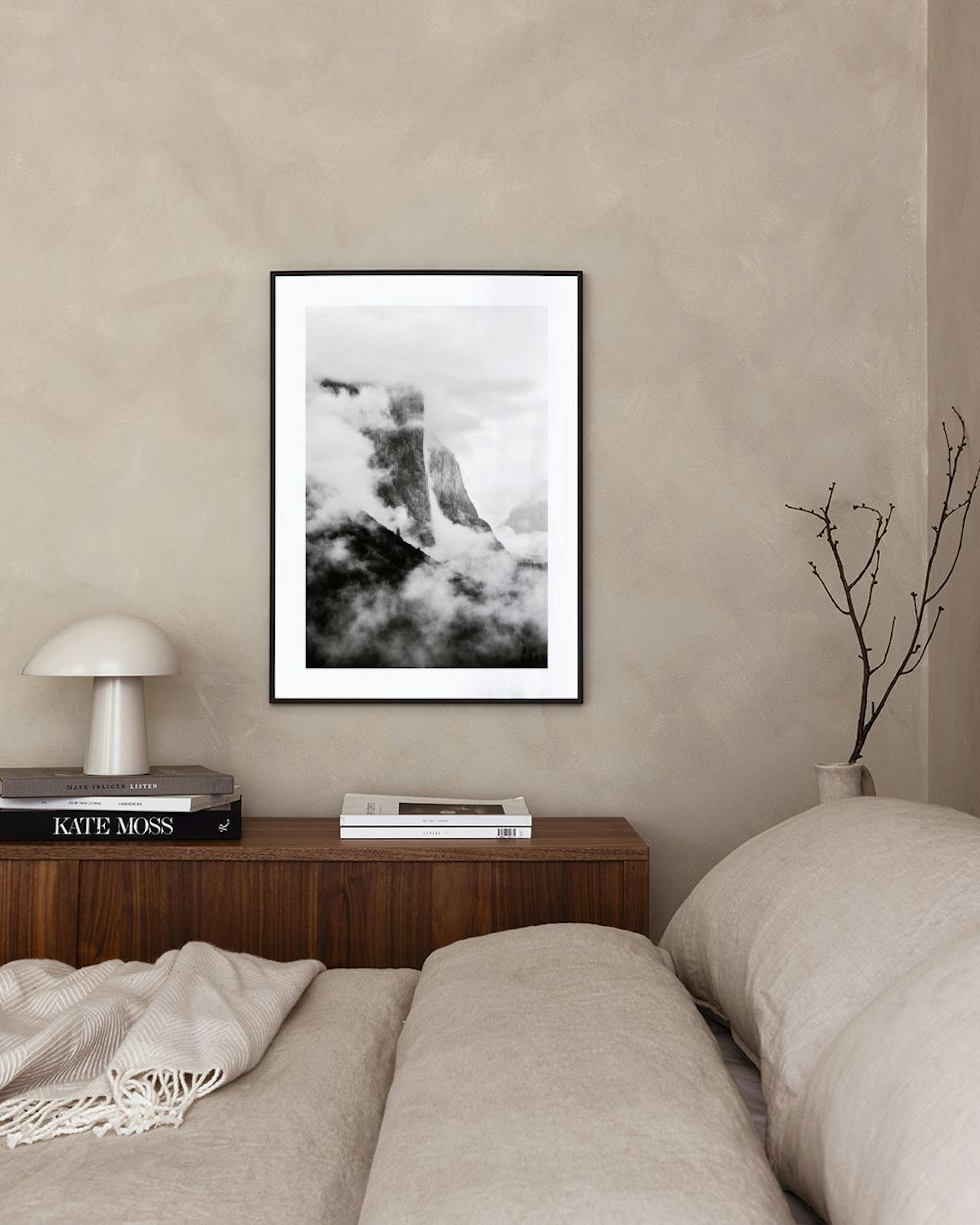 Póster de montaña en blanco y negro con nubes bajas, exhibido sobre una mesa redonda negra y un puf en una sala moderna.