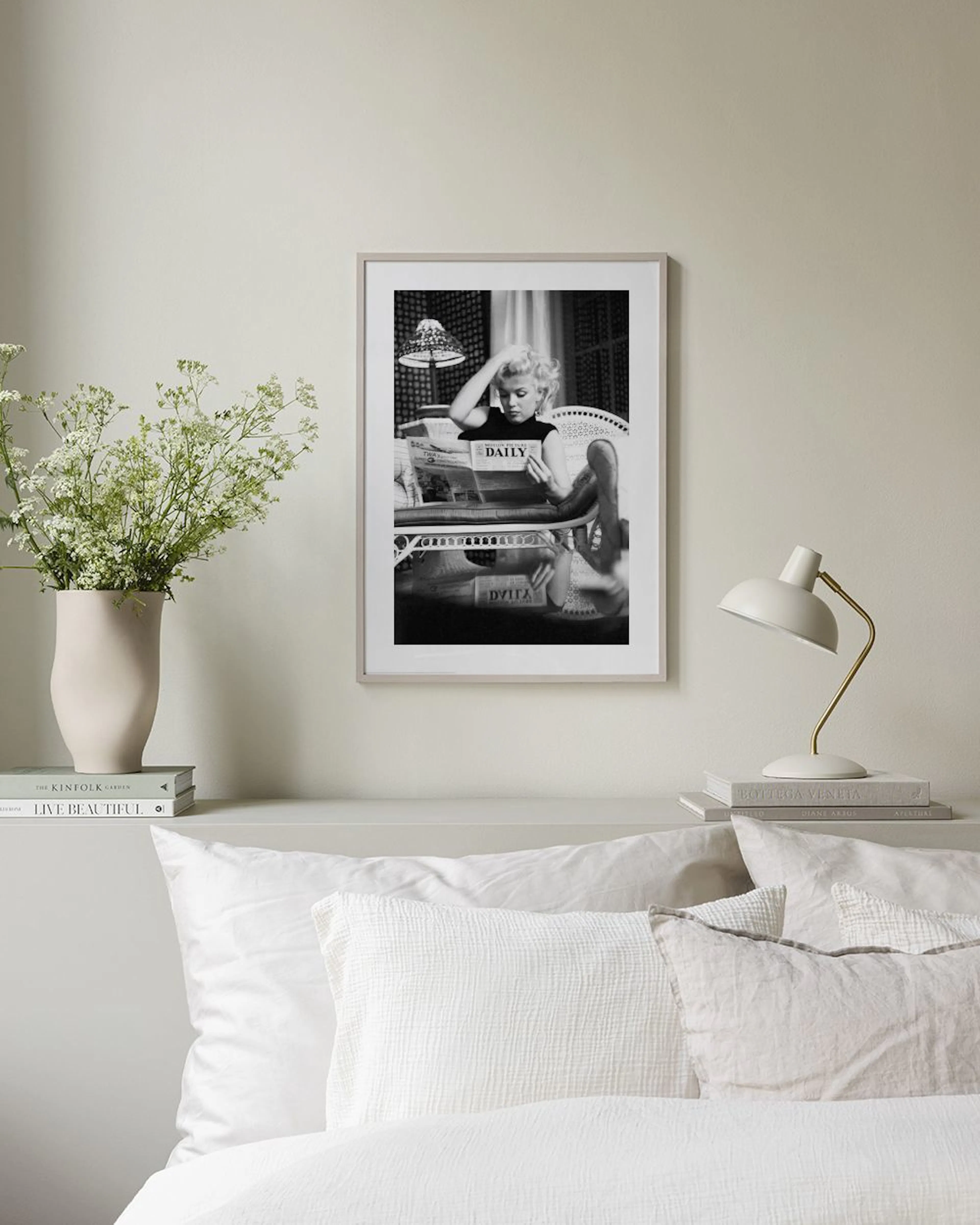 Plakat med svart-hvitt bilde av Marilyn Monroe som leser avisen i en lenestol, henger over et svart konsollbord.
